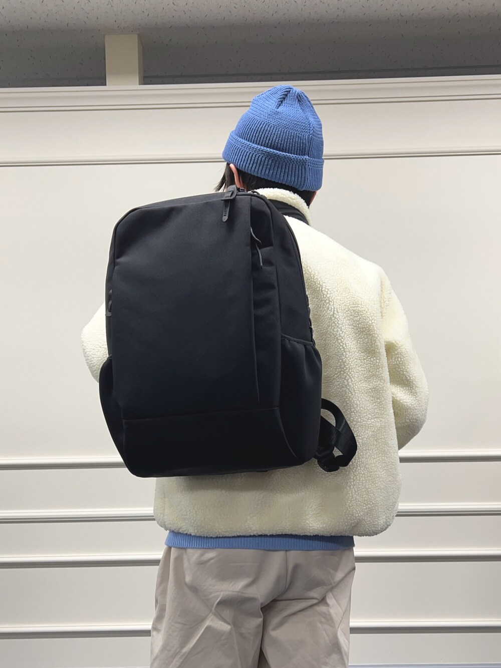 ブルー系のニット/セーター、ホワイト系のブルゾン、ブラック系のバックパック/リュックを着用したメンズの秋コーディネートの8枚目の写真