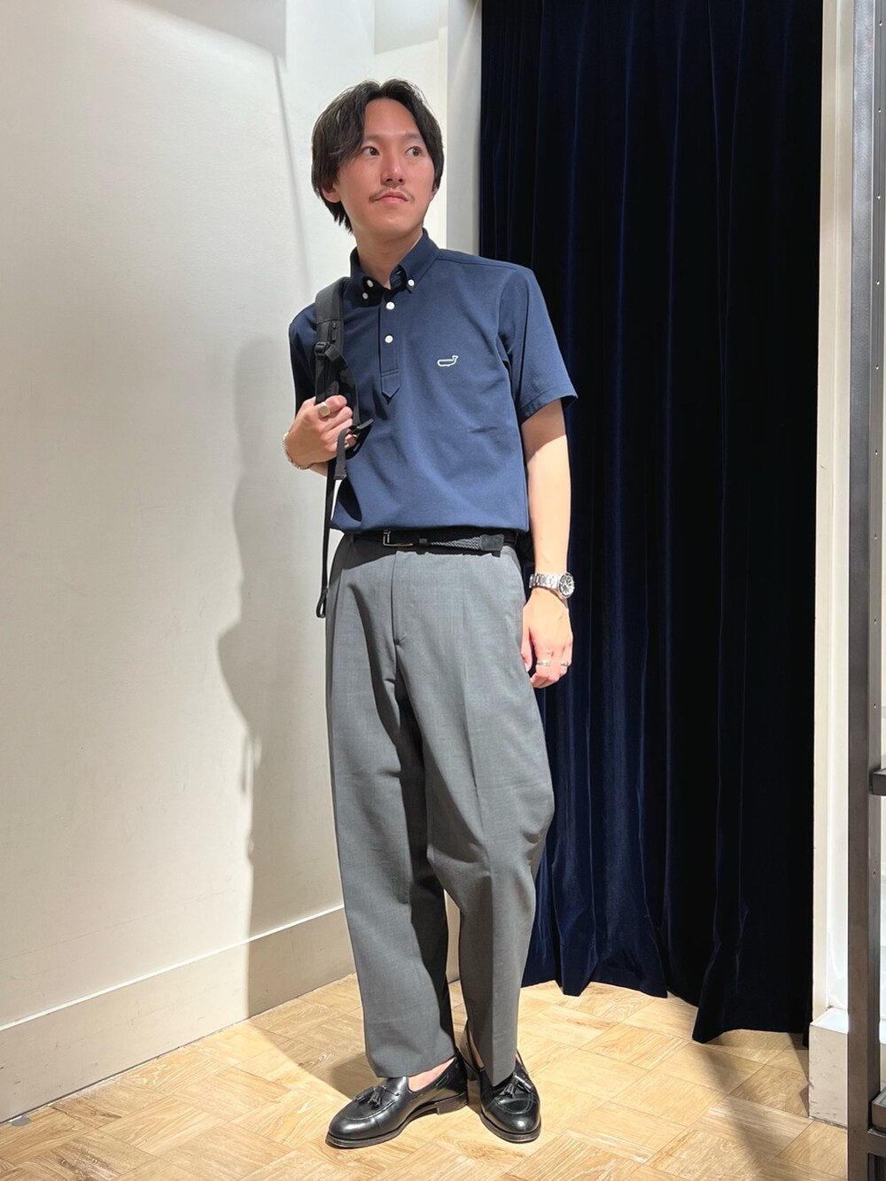 ブルー系のポロシャツ、ブラック系のバックパック/リュック、ブラック系のベルトを着用したメンズの夏コーディネートの2枚目の写真