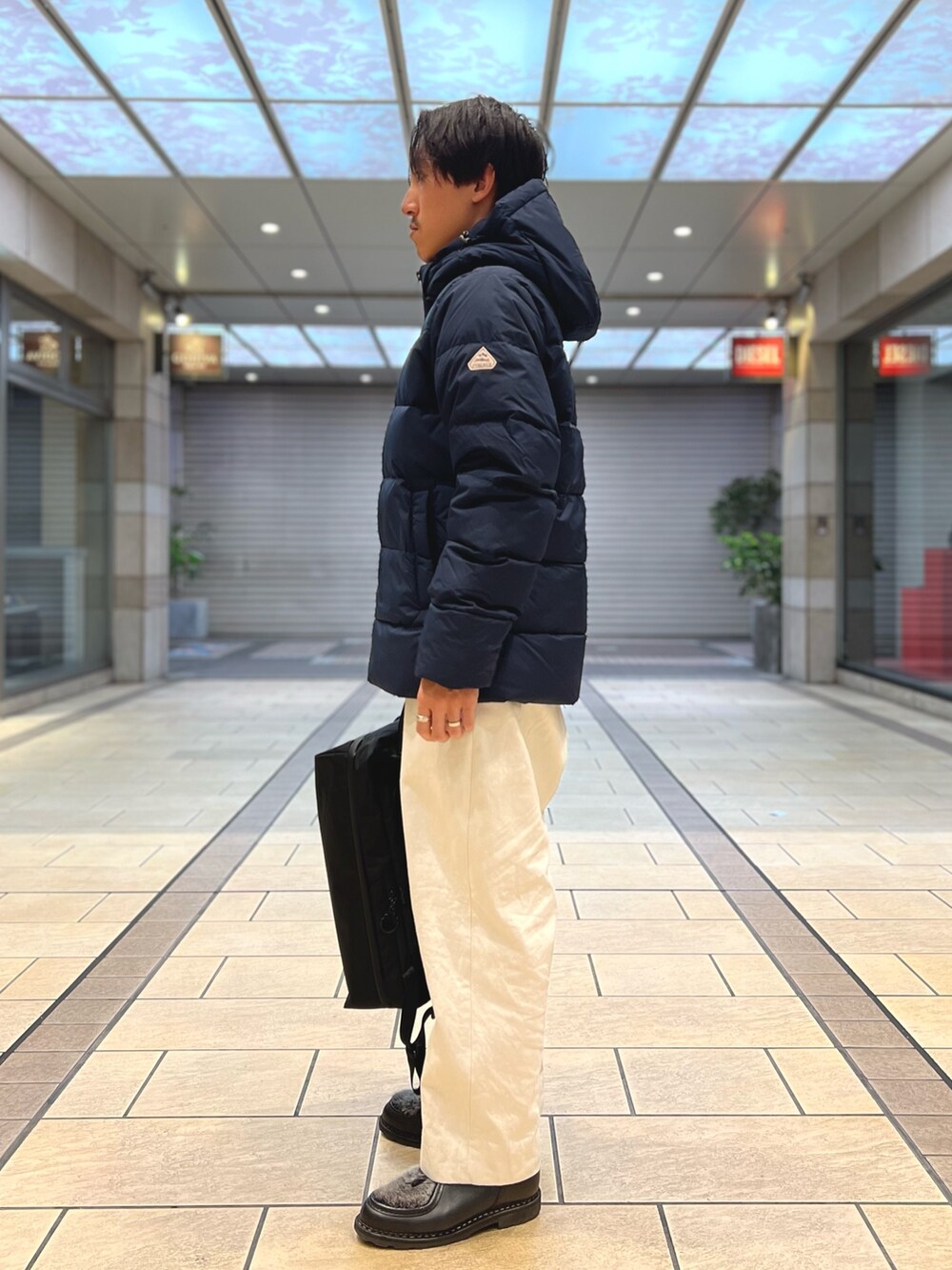 ブラック系のダウンジャケット/コート、ブラック系のバックパック/リュック、ブルー系のシャツ/ブラウスを着用したメンズの春コーディネートの3枚目の写真