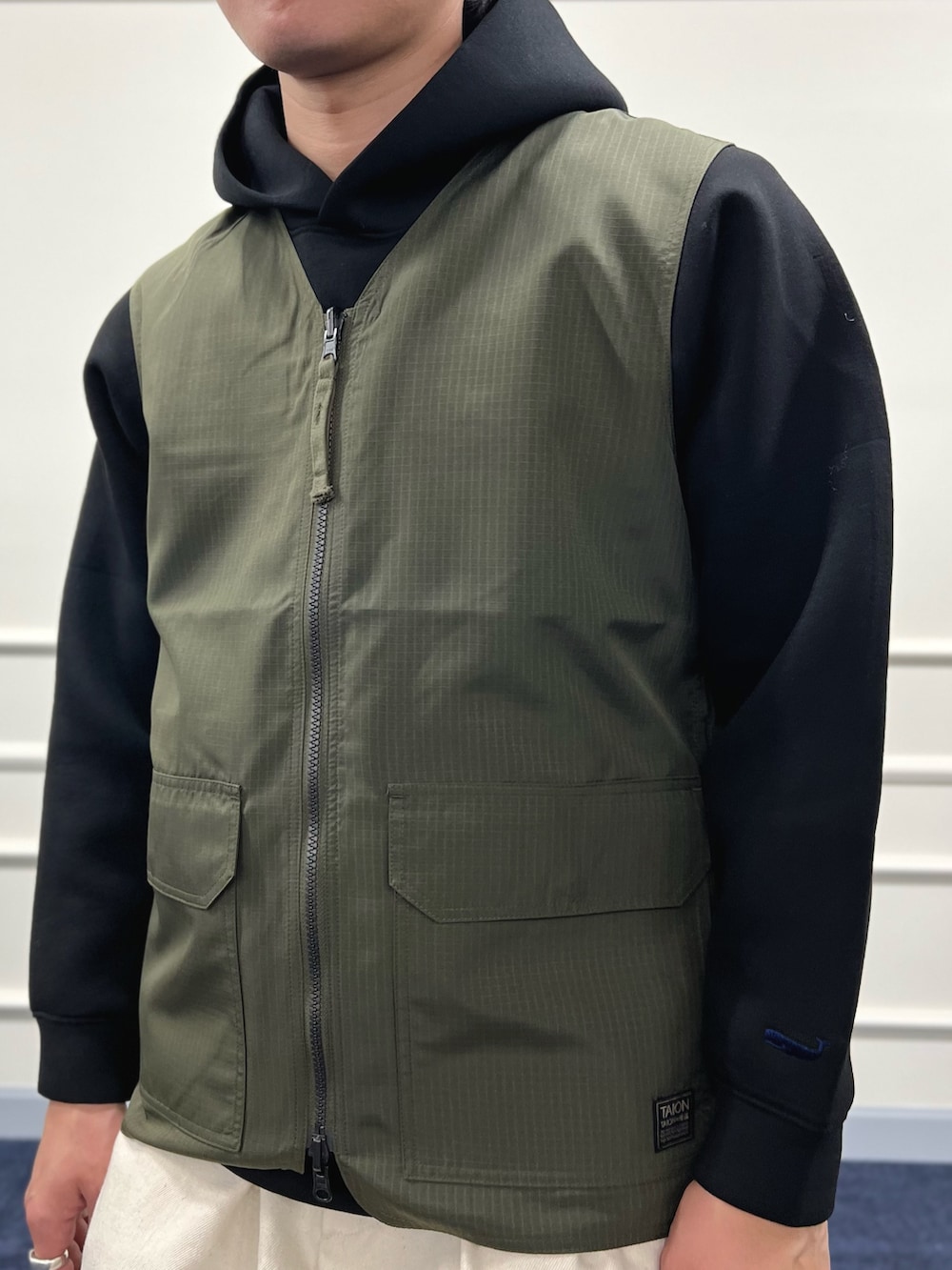 グリーン系のベスト、ブラック系のパーカー、ホワイト系のデニムパンツを着用したメンズの冬コーディネートの9枚目の写真