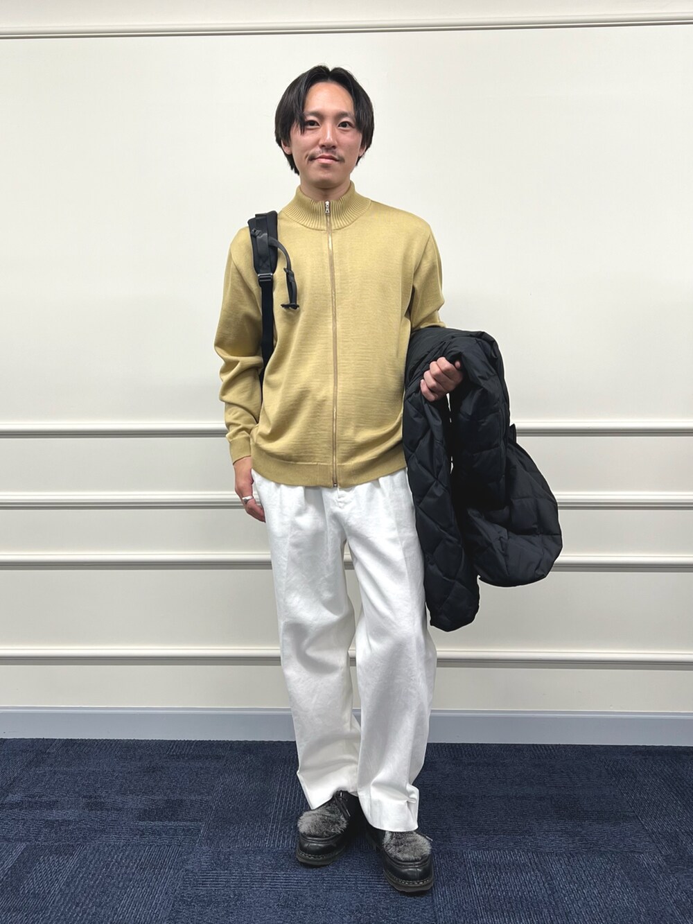 ブラック系のダウンジャケット/コート、ブラック系のバックパック/リュック、ベージュ系のカーディガン/ボレロを着用したメンズの冬コーディネートの3枚目の写真