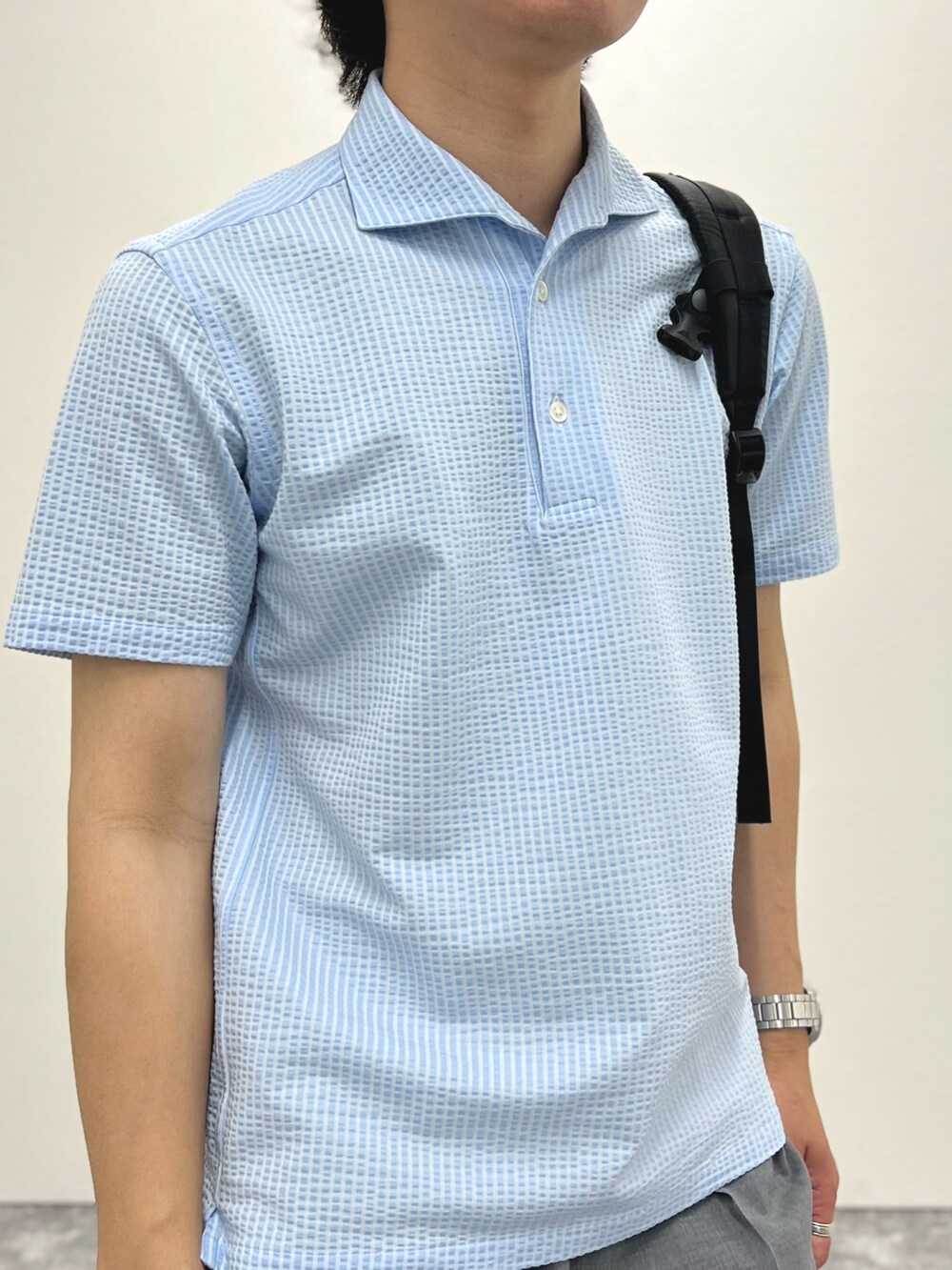 ブルー系のポロシャツ、グレー系のスラックス、ブラック系のバックパック/リュックを着用したメンズの春コーディネートの6枚目の写真