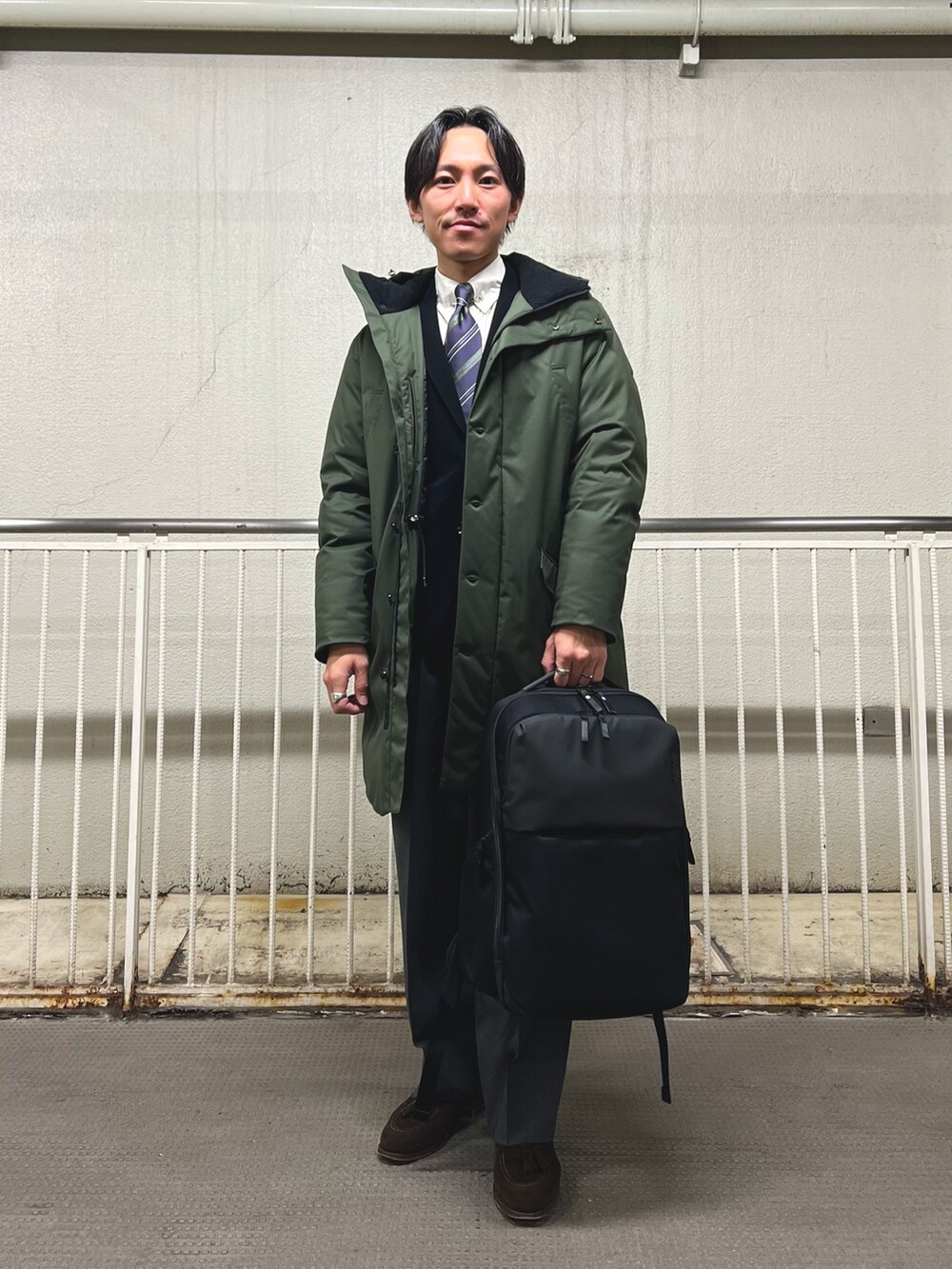 ブルー系のネクタイ、ブラック系のテーラードジャケット、グリーン系のダウンジャケット/コートを着用したメンズの冬コーディネートの2枚目の写真