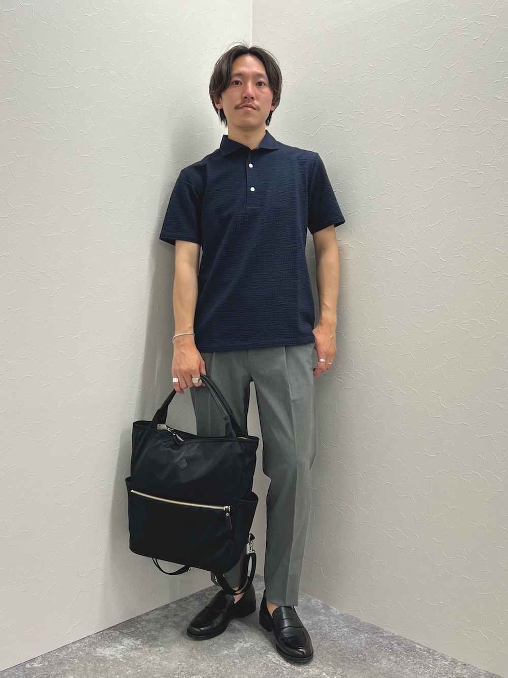 ブルー系のポロシャツ、グレー系のその他パンツ、ブラック系のトートバッグを着用したメンズの夏コーディネートの2枚目の写真