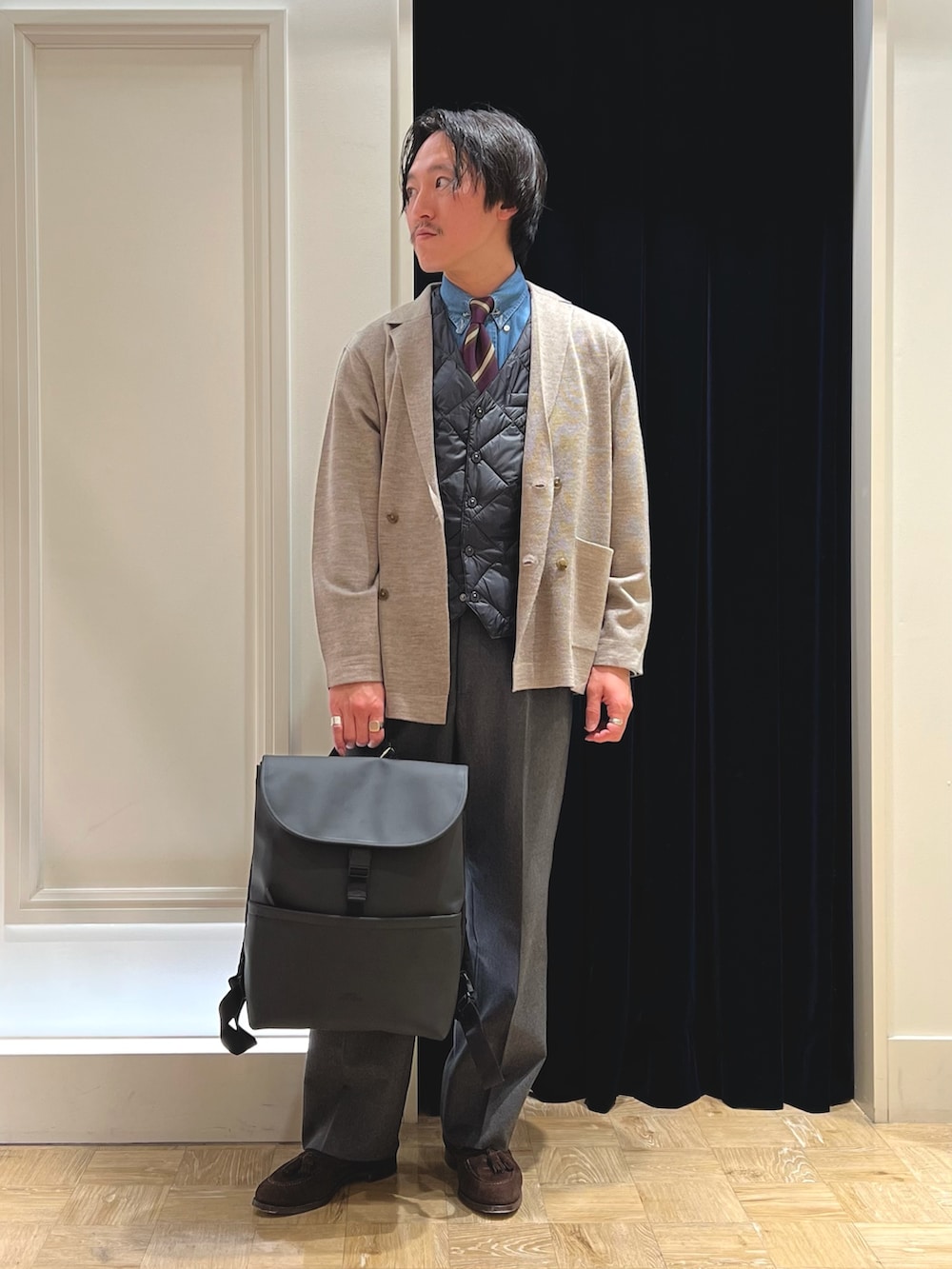 ベージュ系のテーラードジャケット、ブラック系のダウンベスト、ブラック系のバックパック/リュックを着用したメンズの冬コーディネートの3枚目の写真