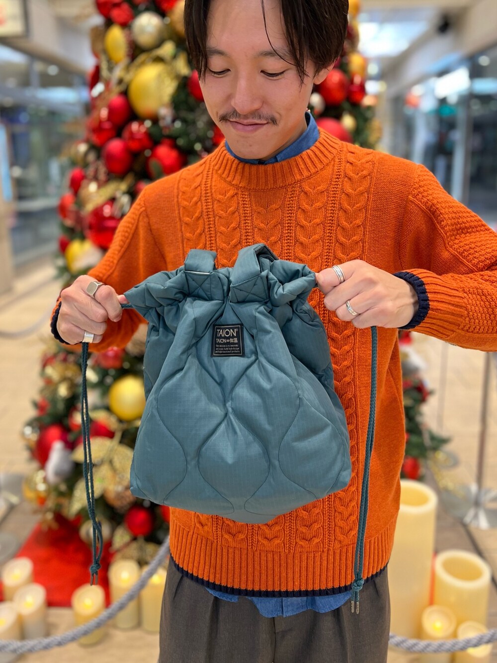 オレンジ系のニット/セーター、ブルー系のシャツ/ブラウス、グリーン系のトートバッグを着用したメンズの冬コーディネートの3枚目の写真