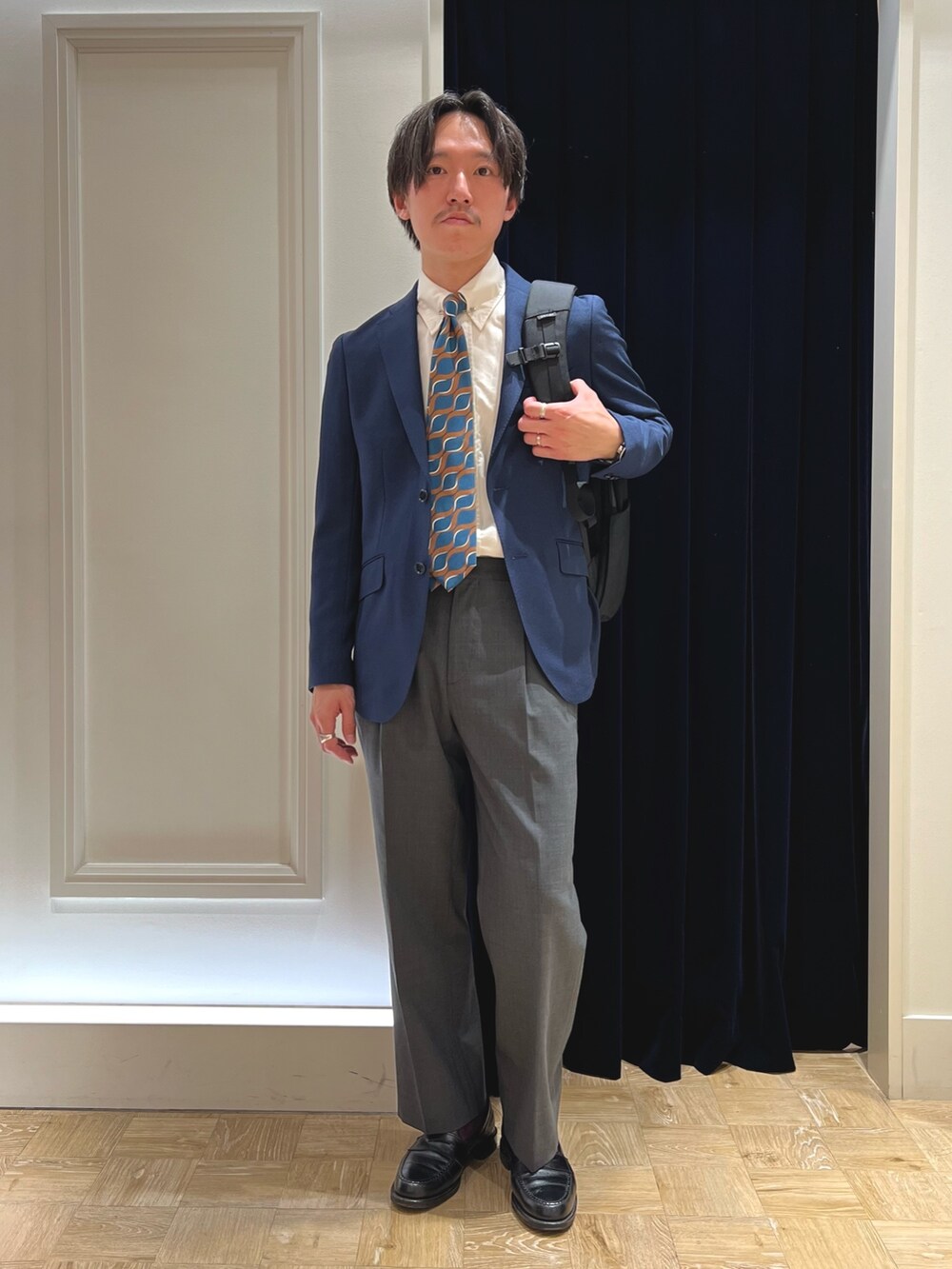 ブルー系のネクタイ、ブルー系のテーラードジャケット、ブラック系のバックパック/リュックを着用したメンズの春コーディネートの4枚目の写真
