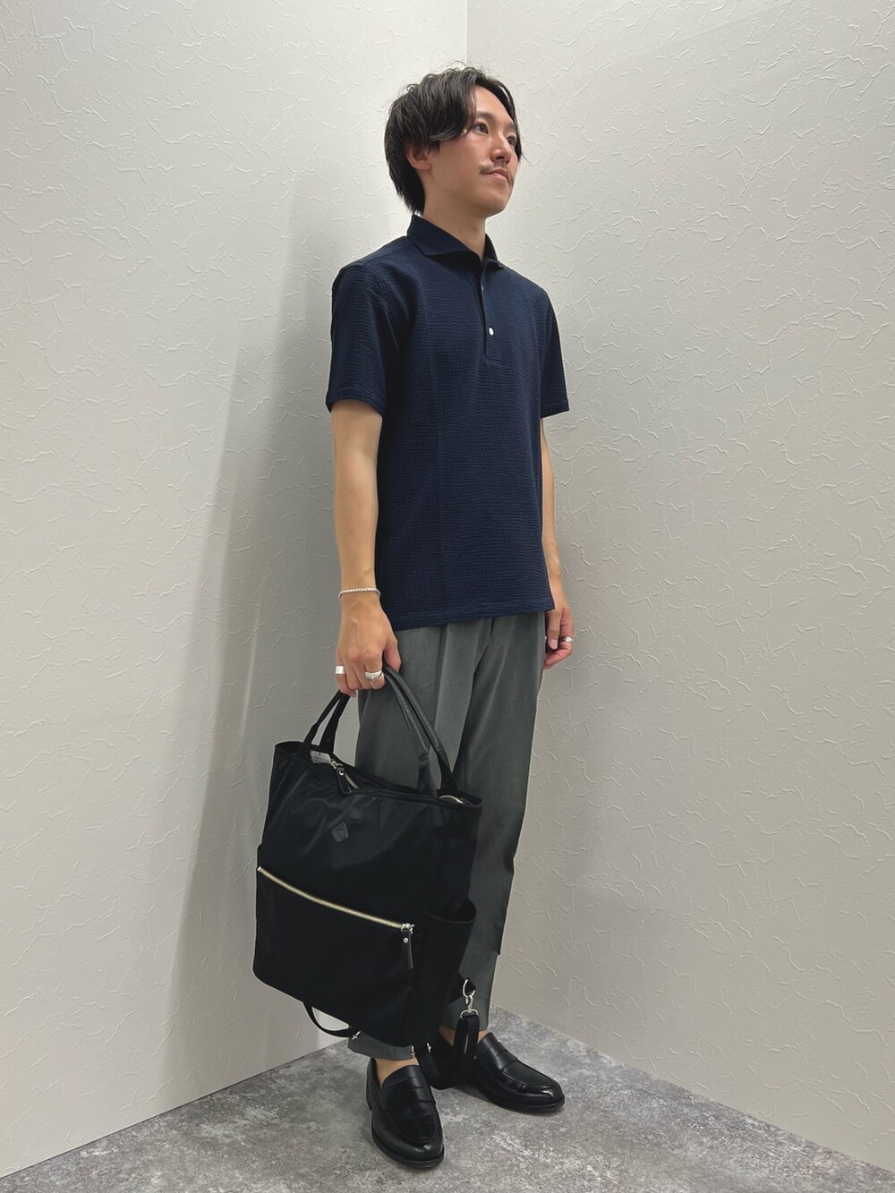 ブルー系のポロシャツ、グレー系のその他パンツ、ブラック系のトートバッグを着用したメンズの夏コーディネートの3枚目の写真