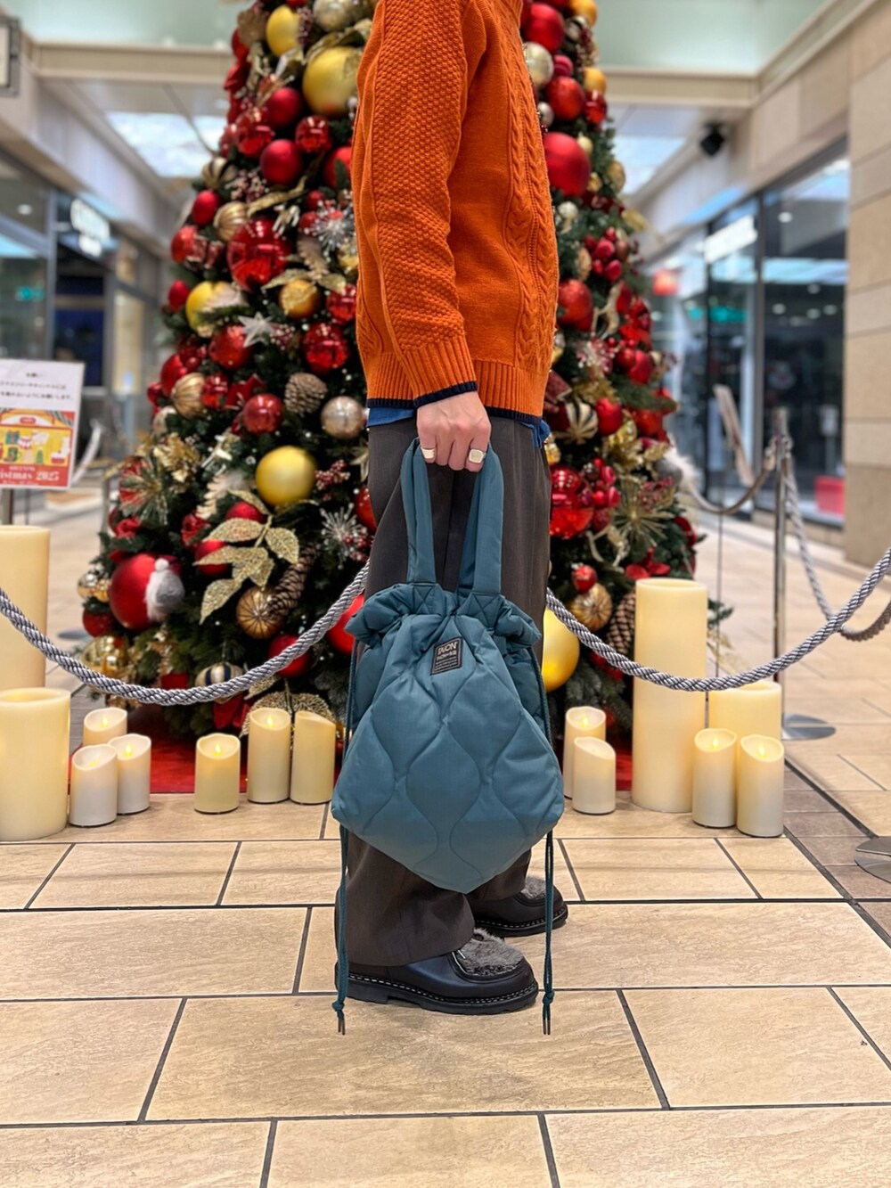 オレンジ系のニット/セーター、ブルー系のシャツ/ブラウス、グリーン系のトートバッグを着用したメンズの冬コーディネートの2枚目の写真