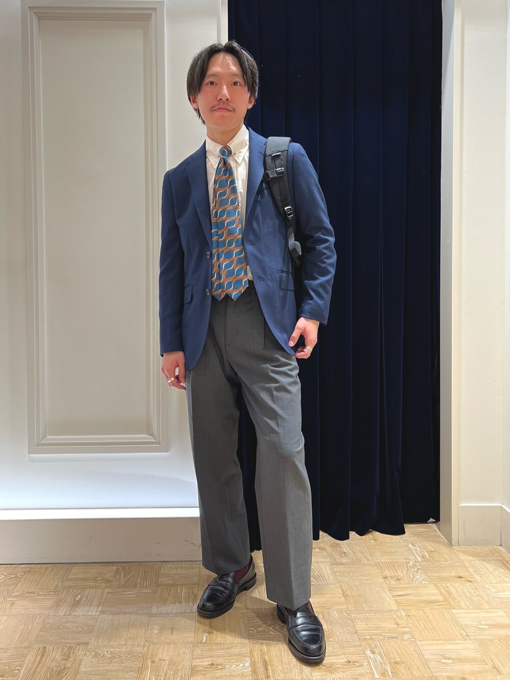 ブルー系のネクタイ、ブルー系のテーラードジャケット、ブラック系のバックパック/リュックを着用したメンズの春コーディネートの3枚目の写真