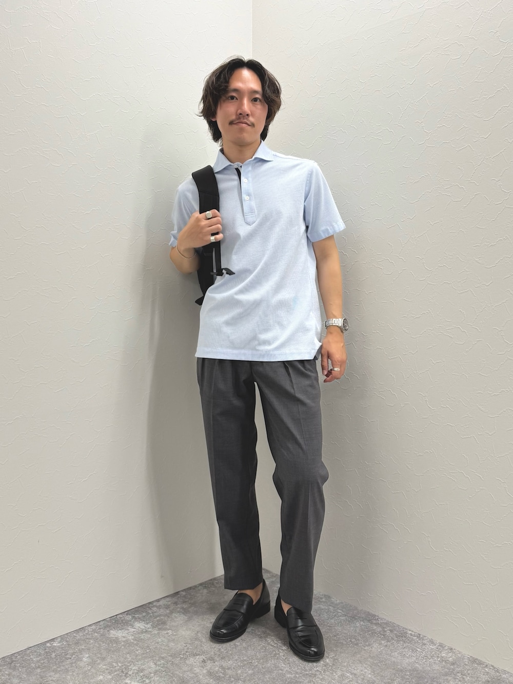 ブルー系のポロシャツ、グレー系のスラックス、ブラック系のバックパック/リュックを着用したメンズの春コーディネートの4枚目の写真
