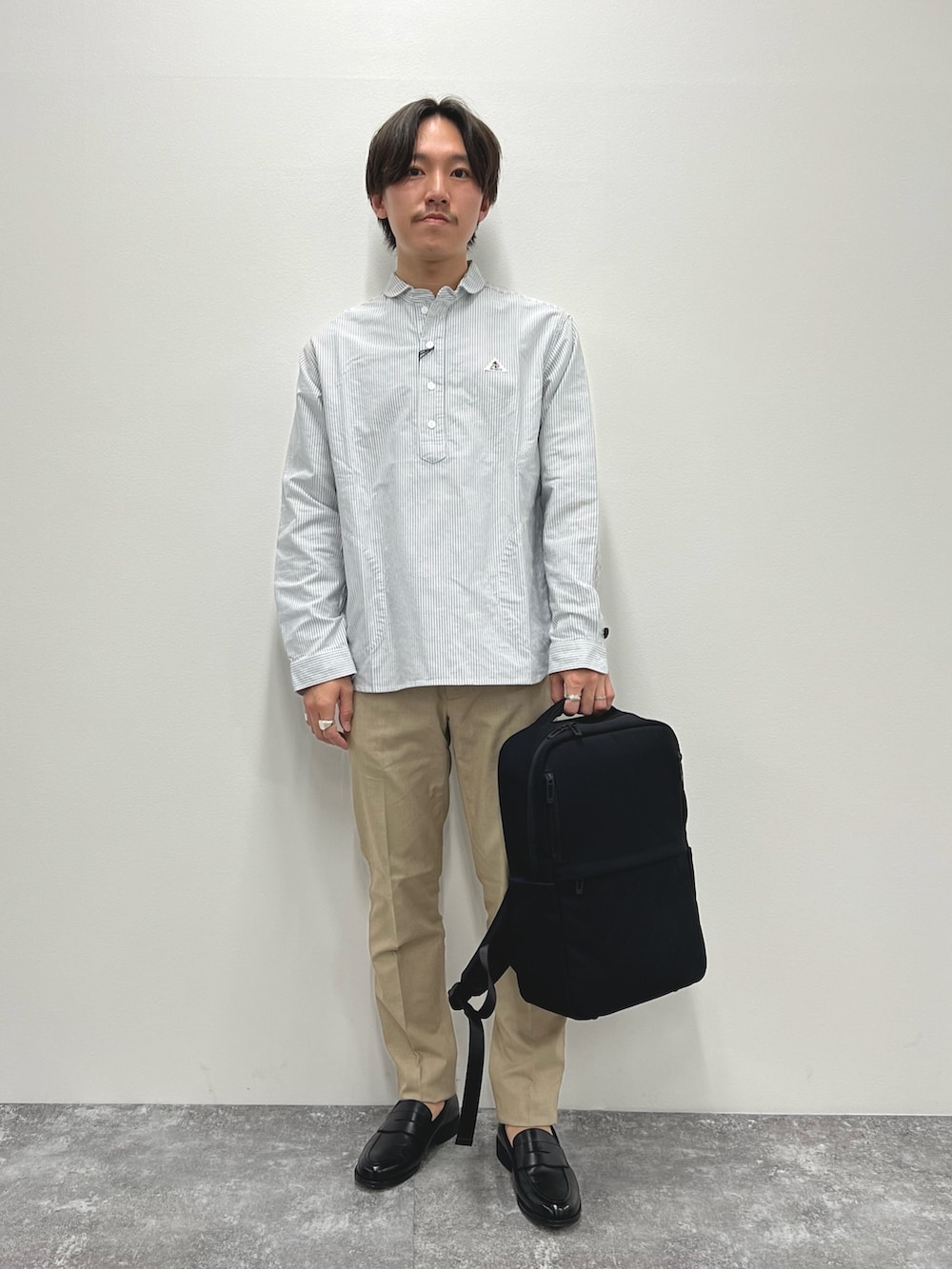 ブラック系のシャツ/ブラウス、ベージュ系のチノパンツ、ブラック系のバックパック/リュックを着用したメンズの春コーディネートの2枚目の写真