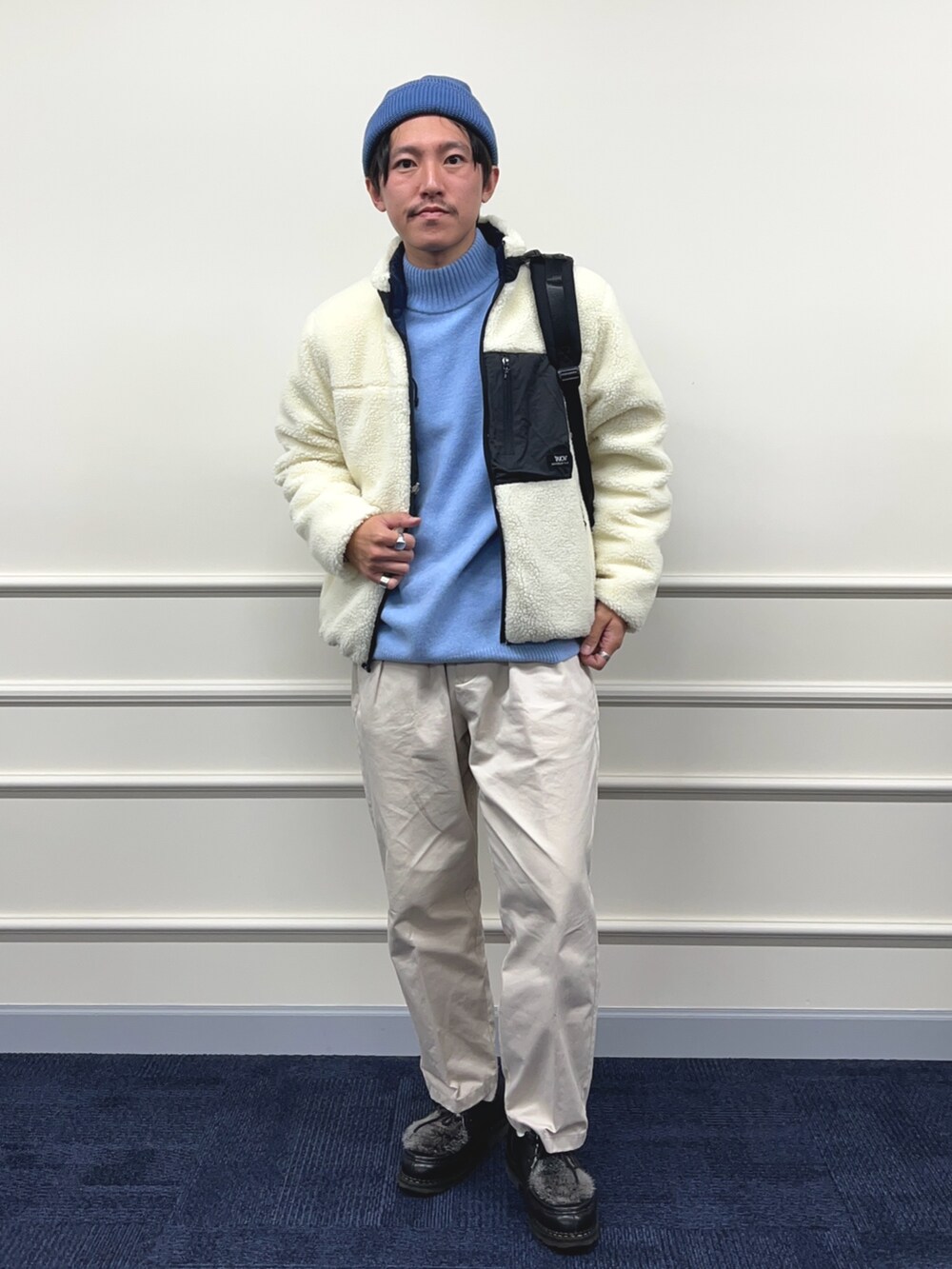 ブルー系のニット/セーター、ホワイト系のブルゾン、ブラック系のバックパック/リュックを着用したメンズの秋コーディネートの2枚目の写真