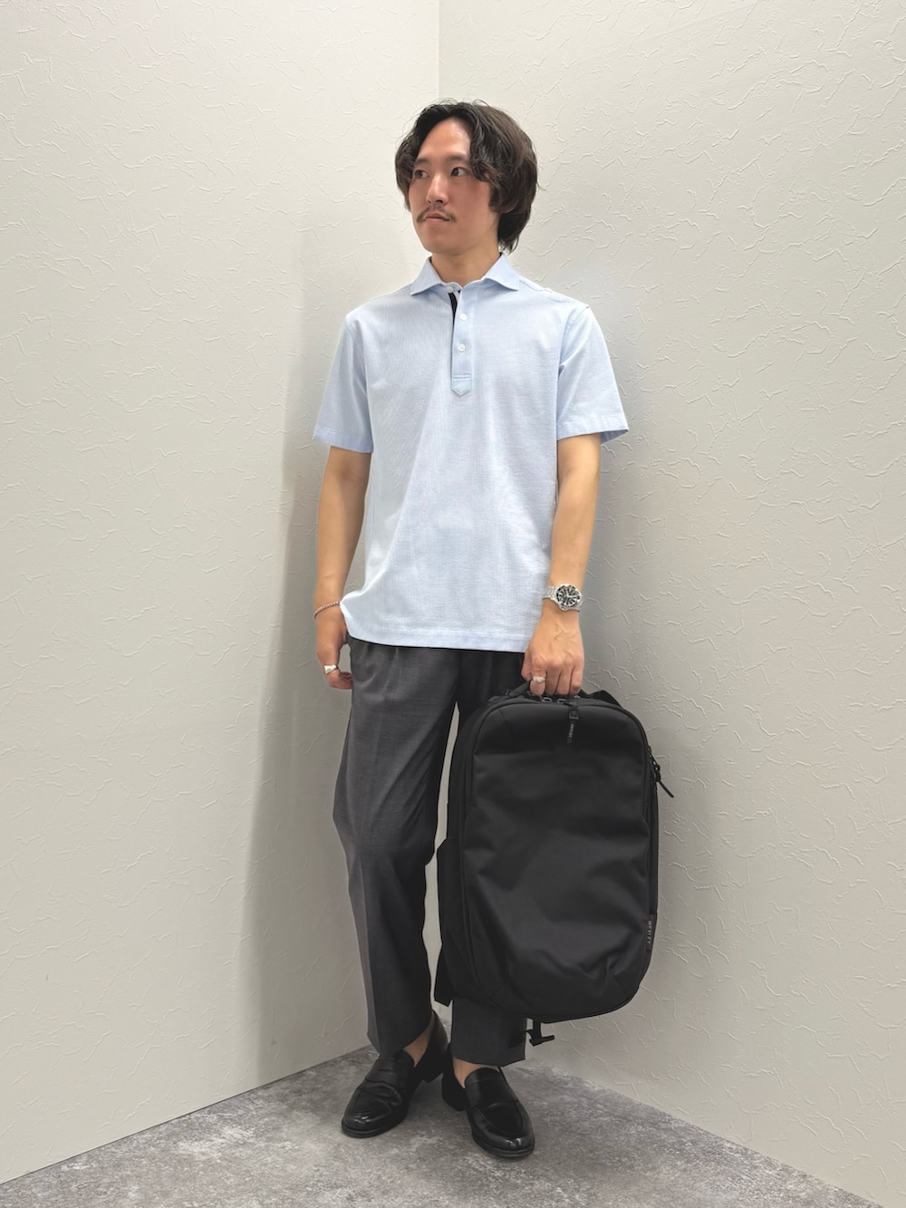 ブルー系のポロシャツ、グレー系のスラックス、ブラック系のバックパック/リュックを着用したメンズの春コーディネートの5枚目の写真