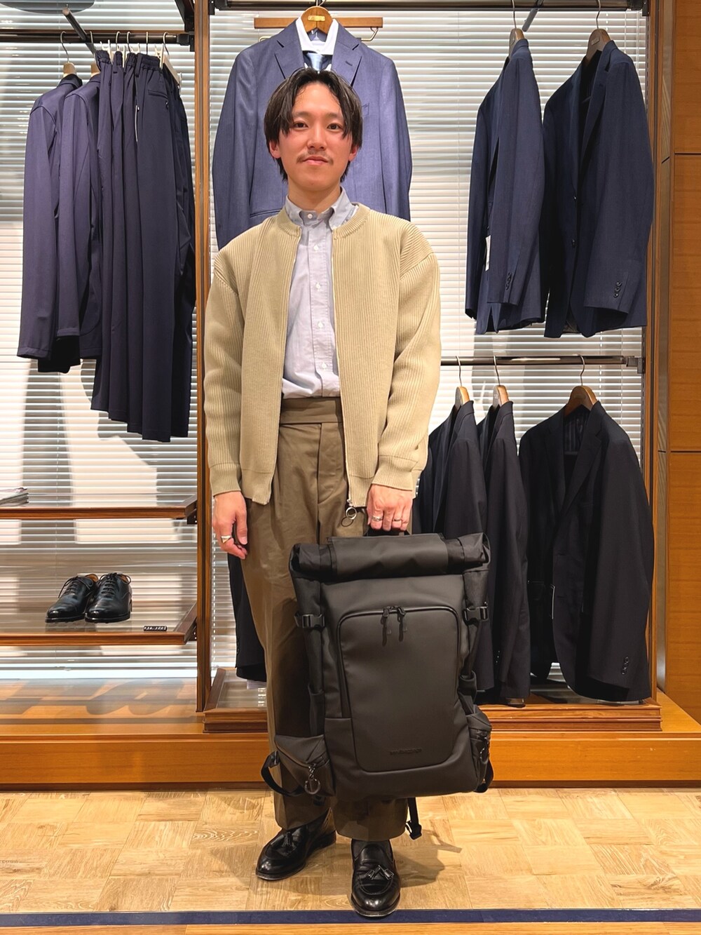ベージュ系のカーディガン/ボレロ、ブラック系のバックパック/リュック、ブラック系のローファーを着用したメンズの春コーディネートの2枚目の写真