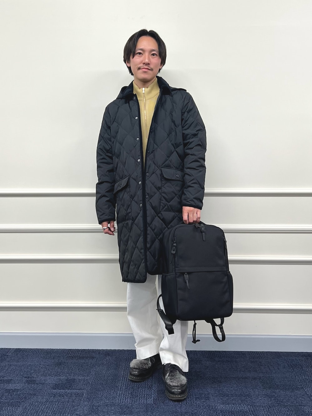 ブラック系のダウンジャケット/コート、ブラック系のバックパック/リュック、ベージュ系のカーディガン/ボレロを着用したメンズの冬コーディネートの2枚目の写真