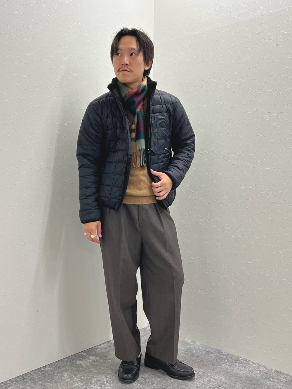 ブラック系のブルゾン、ベージュ系のニット/セーター、グレー系のマフラーを着用したメンズの秋コーディネートの3枚目の写真