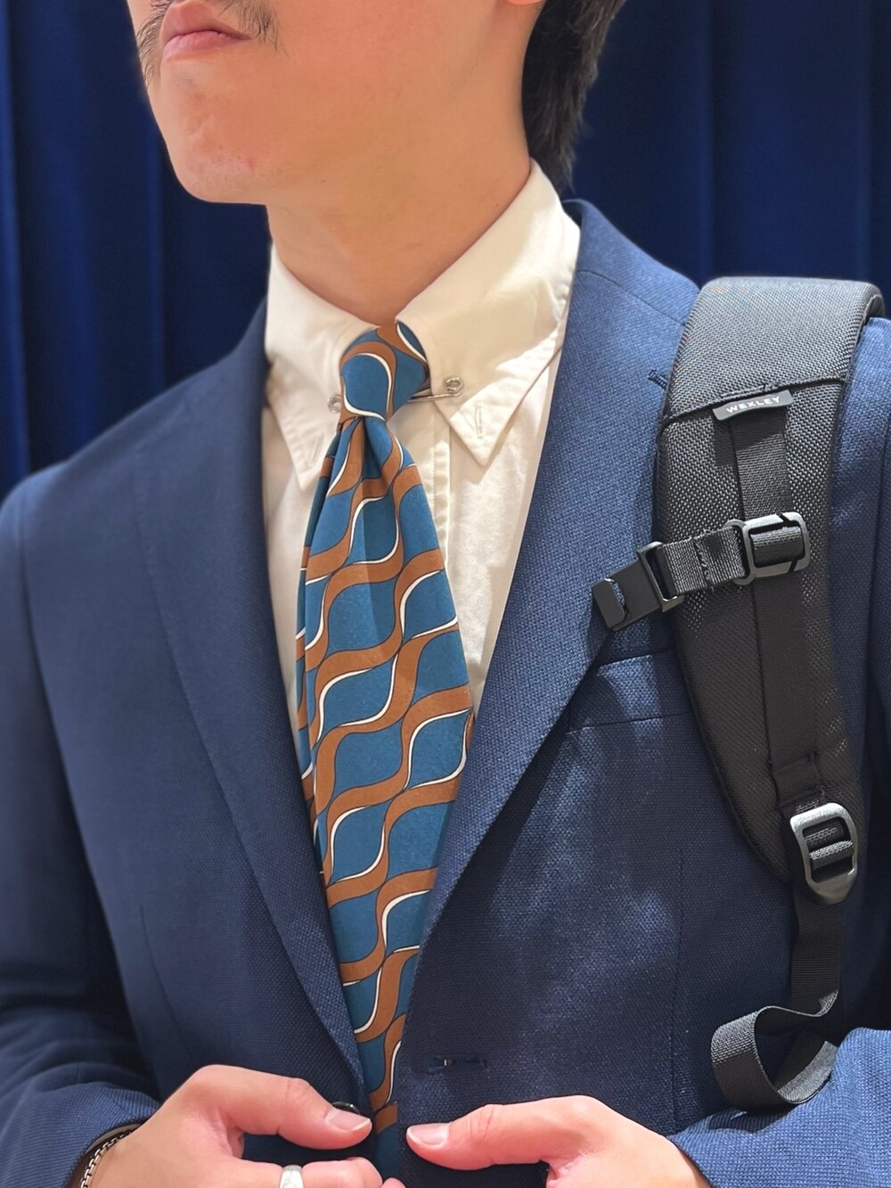 ブルー系のネクタイ、ブルー系のテーラードジャケット、ブラック系のバックパック/リュックを着用したメンズの春コーディネートの8枚目の写真