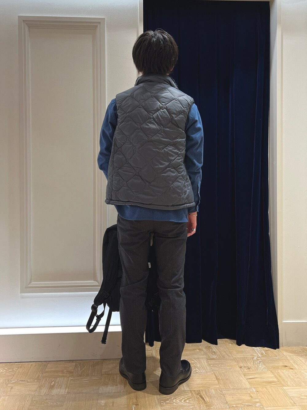 グレー系のダウンベスト、ブルー系のシャツ/ブラウス、ブラック系のバックパック/リュックを着用したメンズの冬コーディネートの5枚目の写真