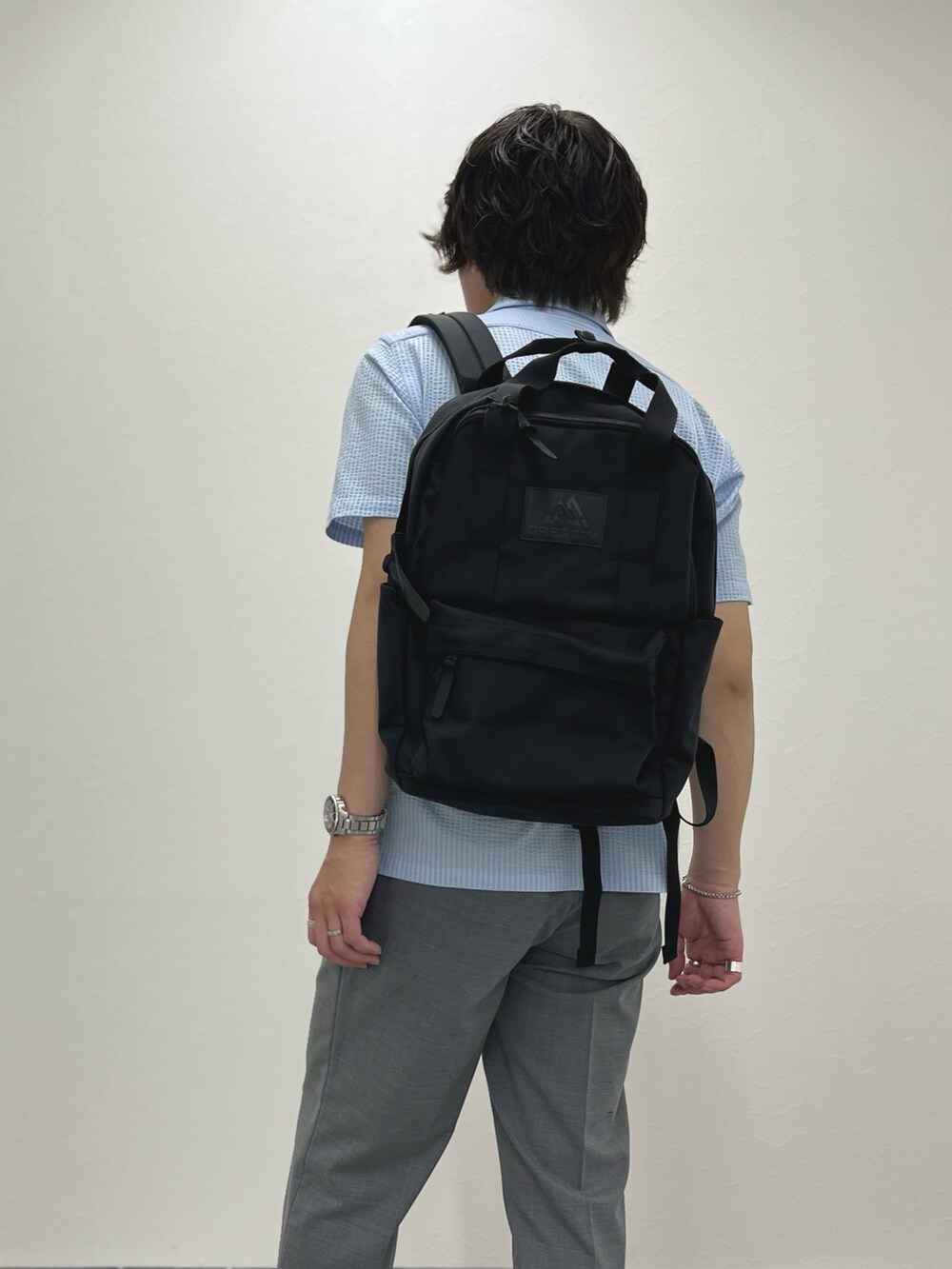 ブルー系のポロシャツ、グレー系のスラックス、ブラック系のバックパック/リュックを着用したメンズの春コーディネートの7枚目の写真