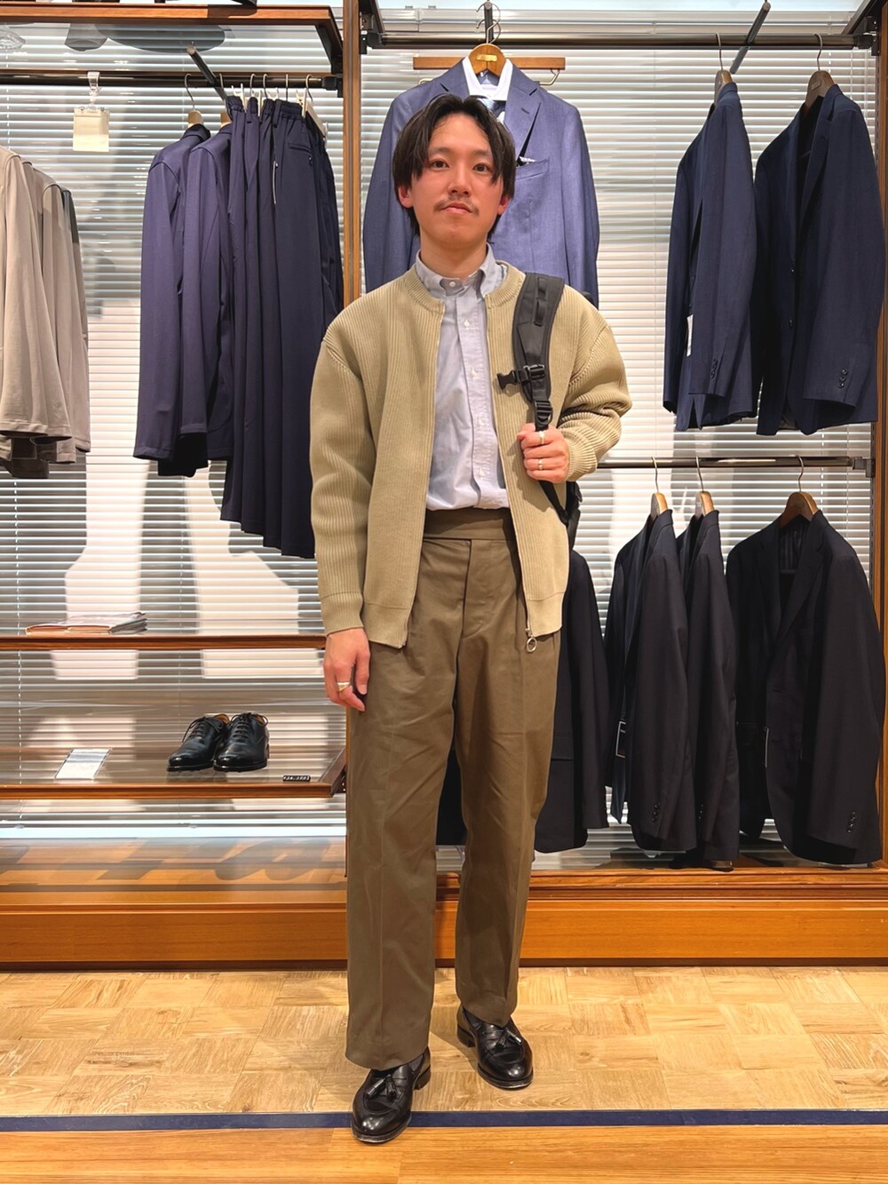 ベージュ系のカーディガン/ボレロ、ブラック系のバックパック/リュック、ブラック系のローファーを着用したメンズの春コーディネートの3枚目の写真