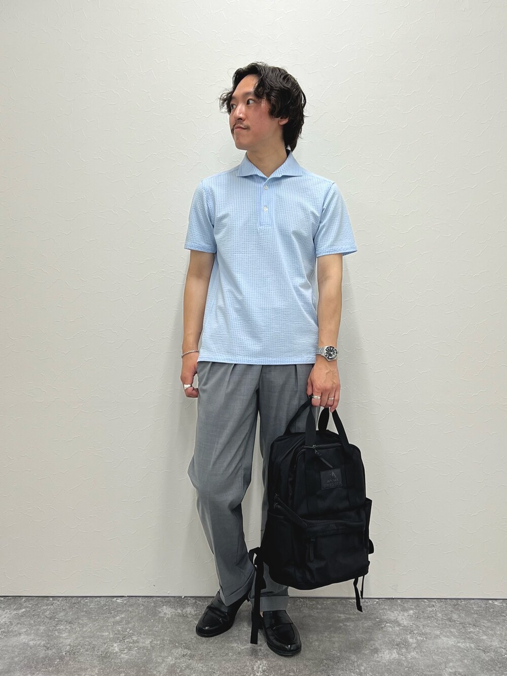 ブルー系のポロシャツ、グレー系のスラックス、ブラック系のバックパック/リュックを着用したメンズの春コーディネートの2枚目の写真