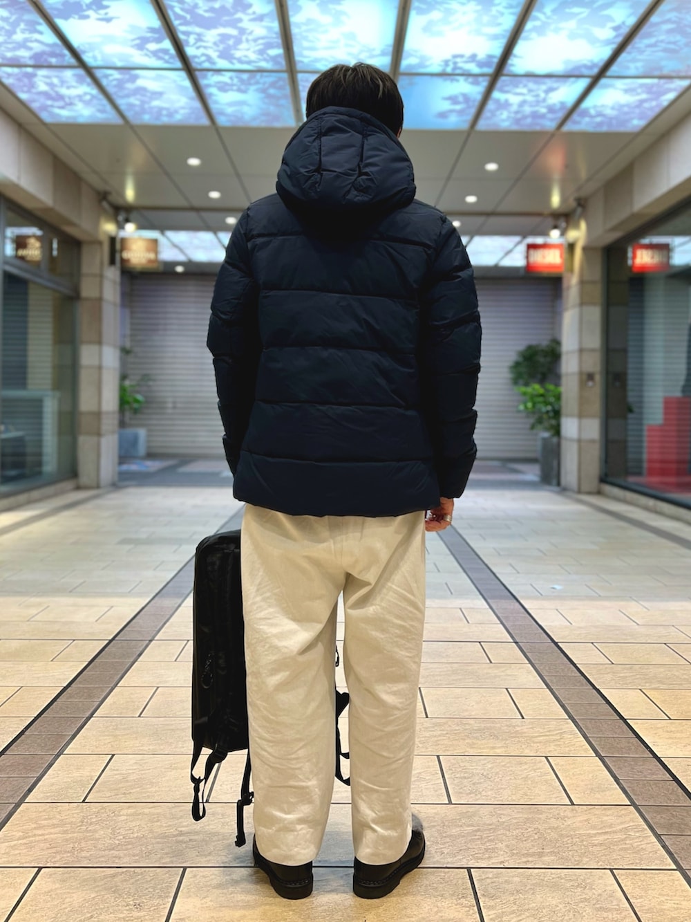 ブラック系のダウンジャケット/コート、ブラック系のバックパック/リュック、ブルー系のシャツ/ブラウスを着用したメンズの春コーディネートの4枚目の写真