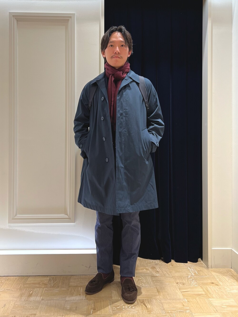 ブルー系のステンカラーコート、ブルー系のその他パンツ、ブラック系のバックパック/リュックを着用したメンズの冬コーディネートの2枚目の写真