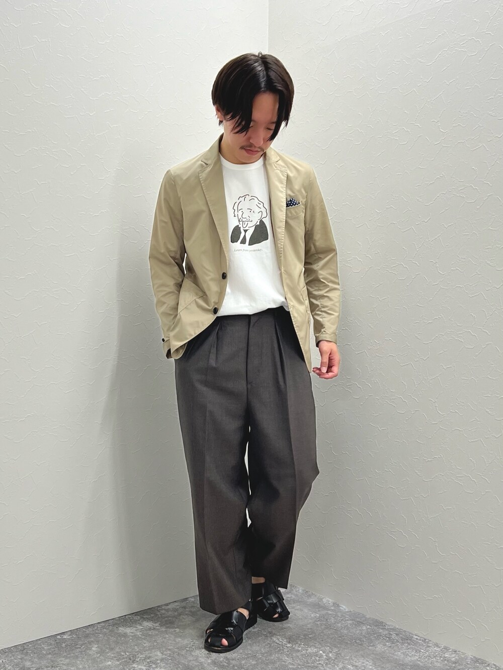ベージュ系のテーラードジャケット、ホワイト系のTシャツ/カットソー、ブラック系のサンダルを着用したメンズの春コーディネートの2枚目の写真
