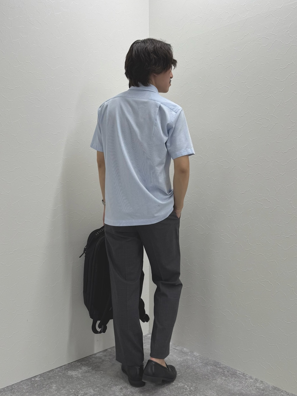 ブルー系のポロシャツ、グレー系のスラックス、ブラック系のバックパック/リュックを着用したメンズの春コーディネートの7枚目の写真