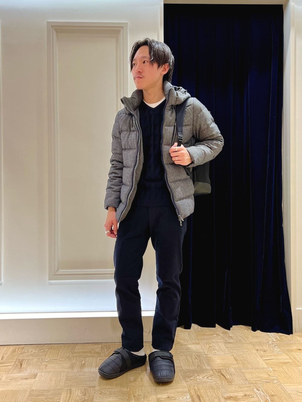 グレー系のダウンジャケット/コート、ブルー系のニット/セーター、ブラック系のバックパック/リュックを着用したメンズの冬コーディネートの2枚目の写真