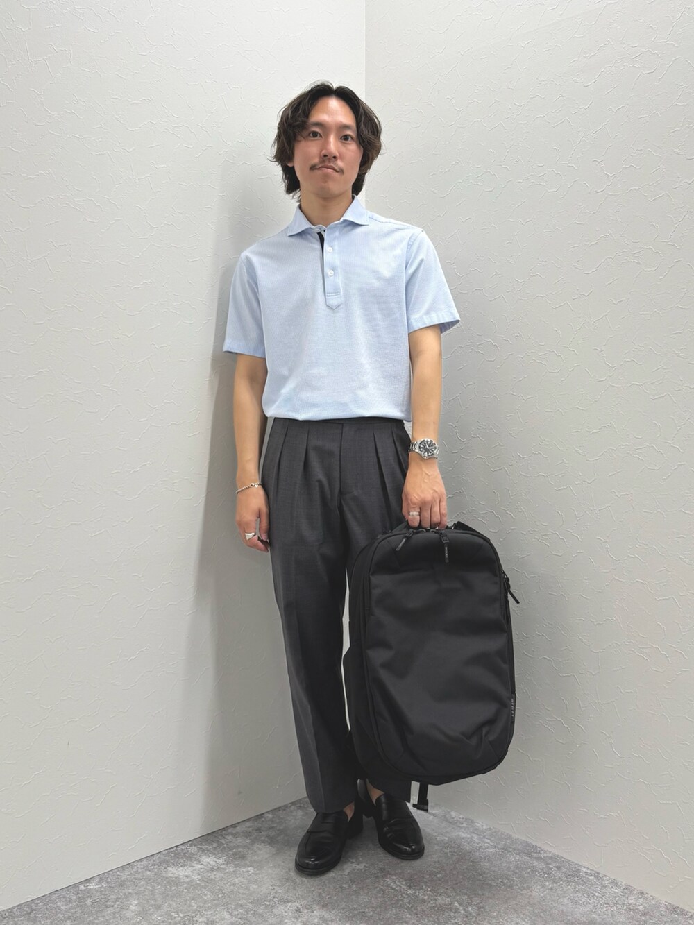 ブルー系のポロシャツ、グレー系のスラックス、ブラック系のバックパック/リュックを着用したメンズの春コーディネートの3枚目の写真