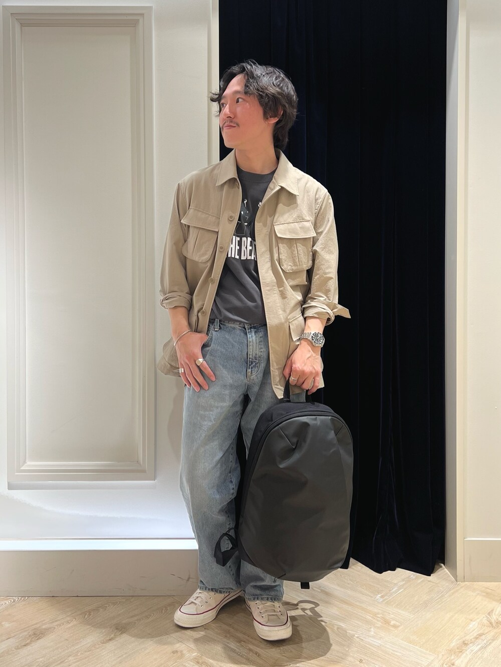 ベージュ系のミリタリージャケット、ブラック系のTシャツ/カットソー、ブラック系のバックパック/リュックを着用したメンズの春コーディネートの2枚目の写真