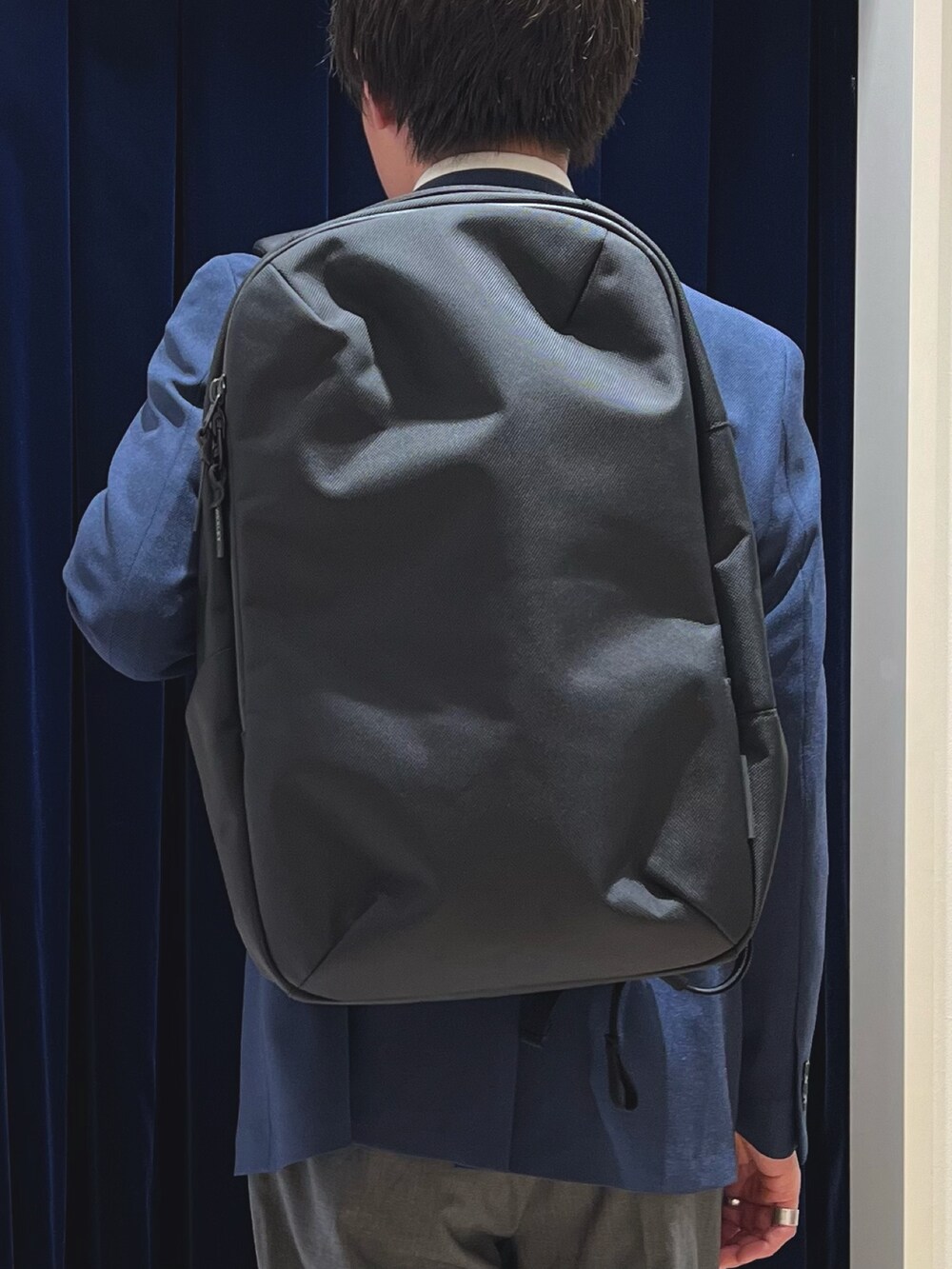 ブルー系のネクタイ、ブルー系のテーラードジャケット、ブラック系のバックパック/リュックを着用したメンズの春コーディネートの7枚目の写真