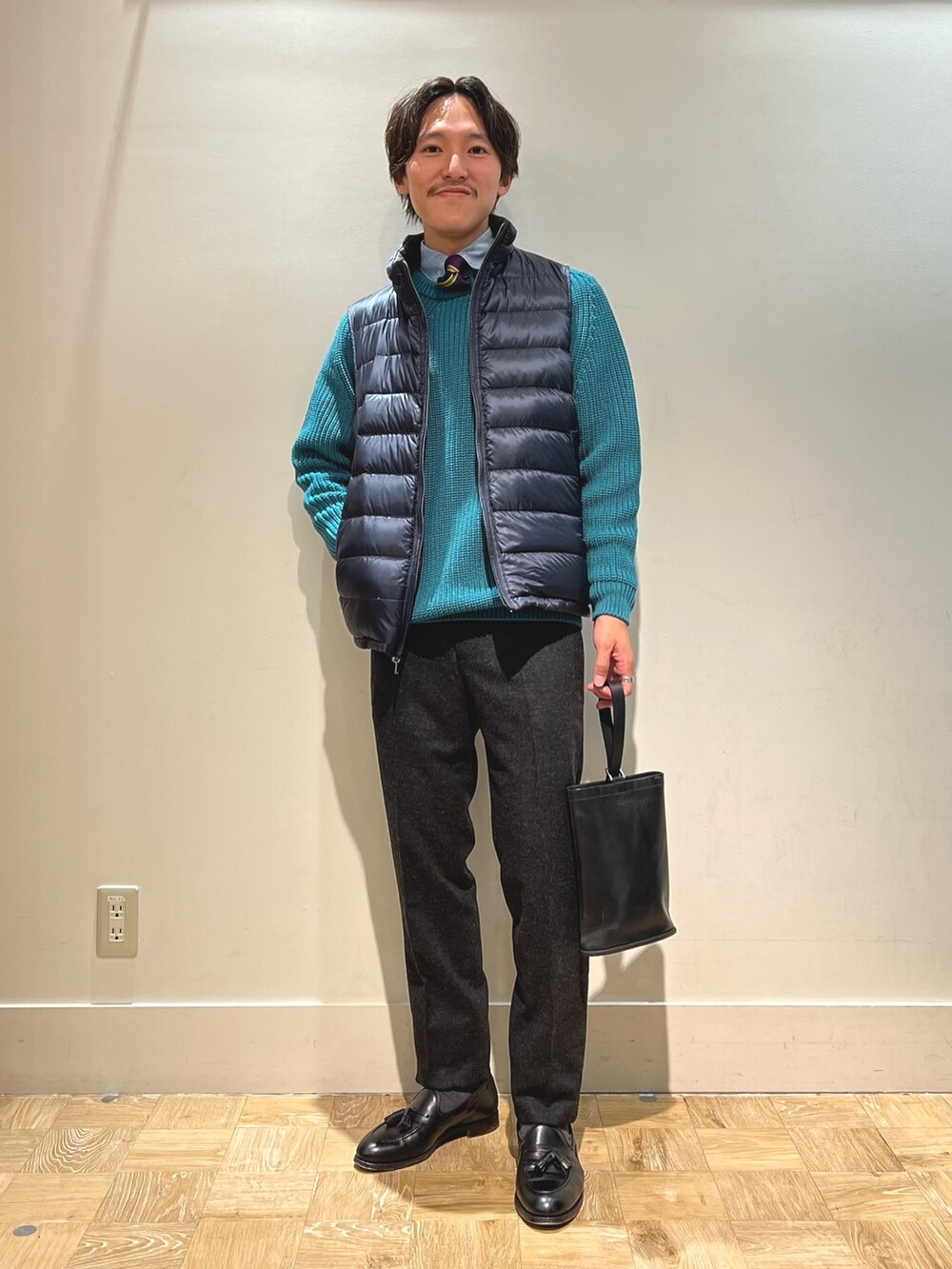 ブラウン系のダウンベスト、ブラック系のハンドバッグを着用したメンズの春コーディネートの3枚目の写真