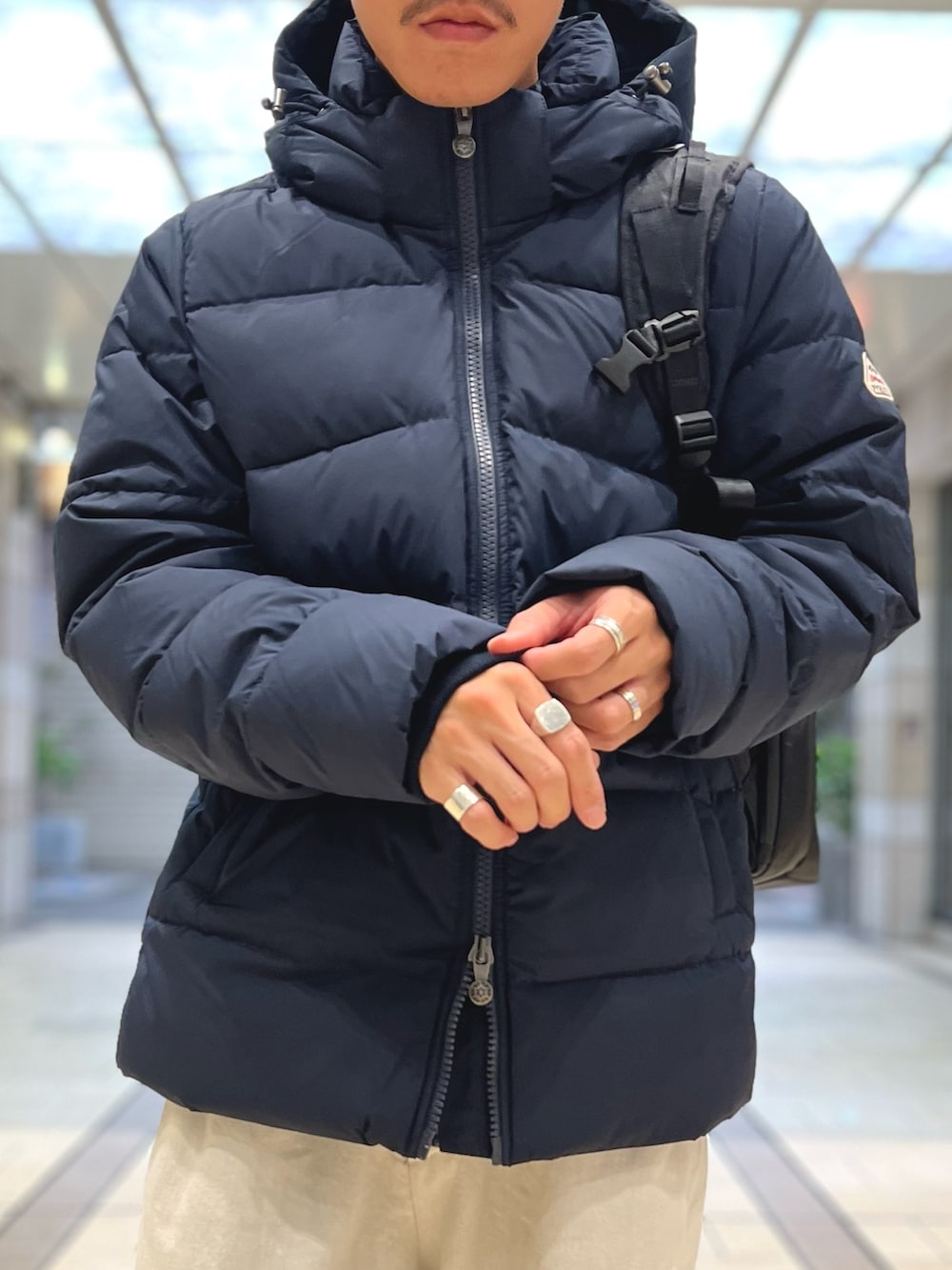 ブラック系のダウンジャケット/コート、ブラック系のバックパック/リュック、ブルー系のシャツ/ブラウスを着用したメンズの春コーディネートの6枚目の写真