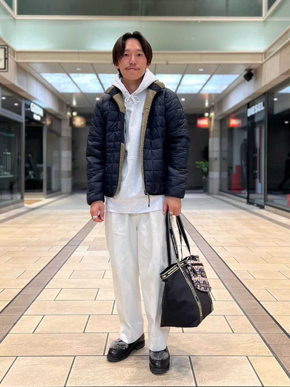 ベージュ系のダウンジャケット/コート、グレー系のパーカー、ブラック系のトートバッグを着用したメンズの秋コーディネートの3枚目の写真