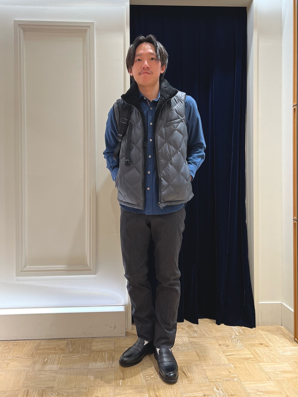 グレー系のダウンベスト、ブルー系のシャツ/ブラウス、ブラック系のバックパック/リュックを着用したメンズの冬コーディネートの2枚目の写真