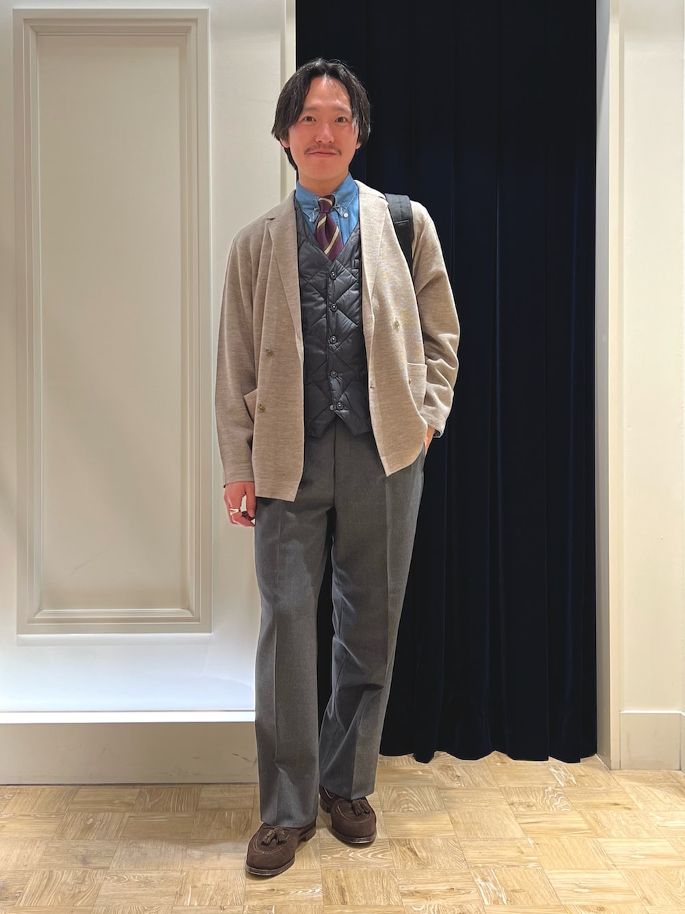 ベージュ系のテーラードジャケット、ブラック系のダウンベスト、ブラック系のバックパック/リュックを着用したメンズの冬コーディネートの2枚目の写真