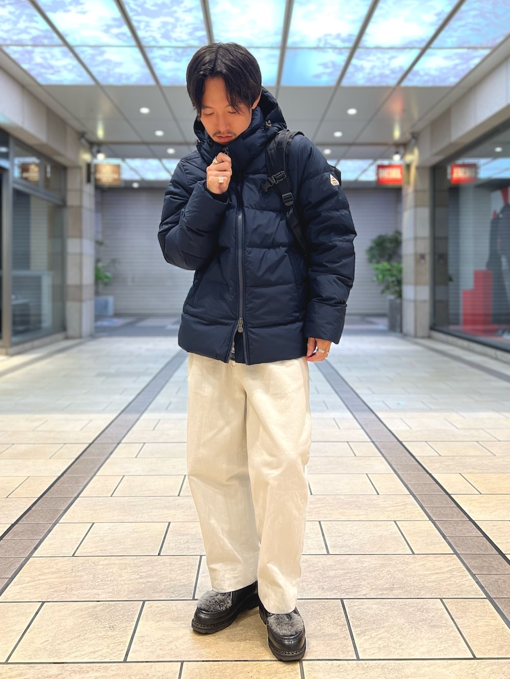 ブラック系のダウンジャケット/コート、ブラック系のバックパック/リュック、ブルー系のシャツ/ブラウスを着用したメンズの春コーディネートの2枚目の写真