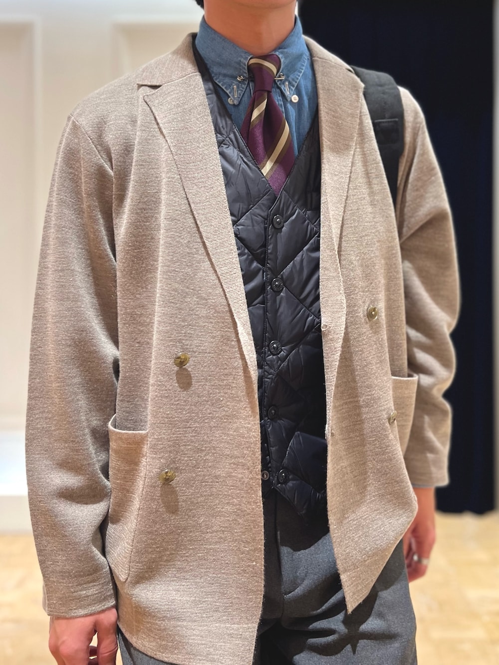 ベージュ系のテーラードジャケット、ブラック系のダウンベスト、ブラック系のバックパック/リュックを着用したメンズの冬コーディネートの9枚目の写真