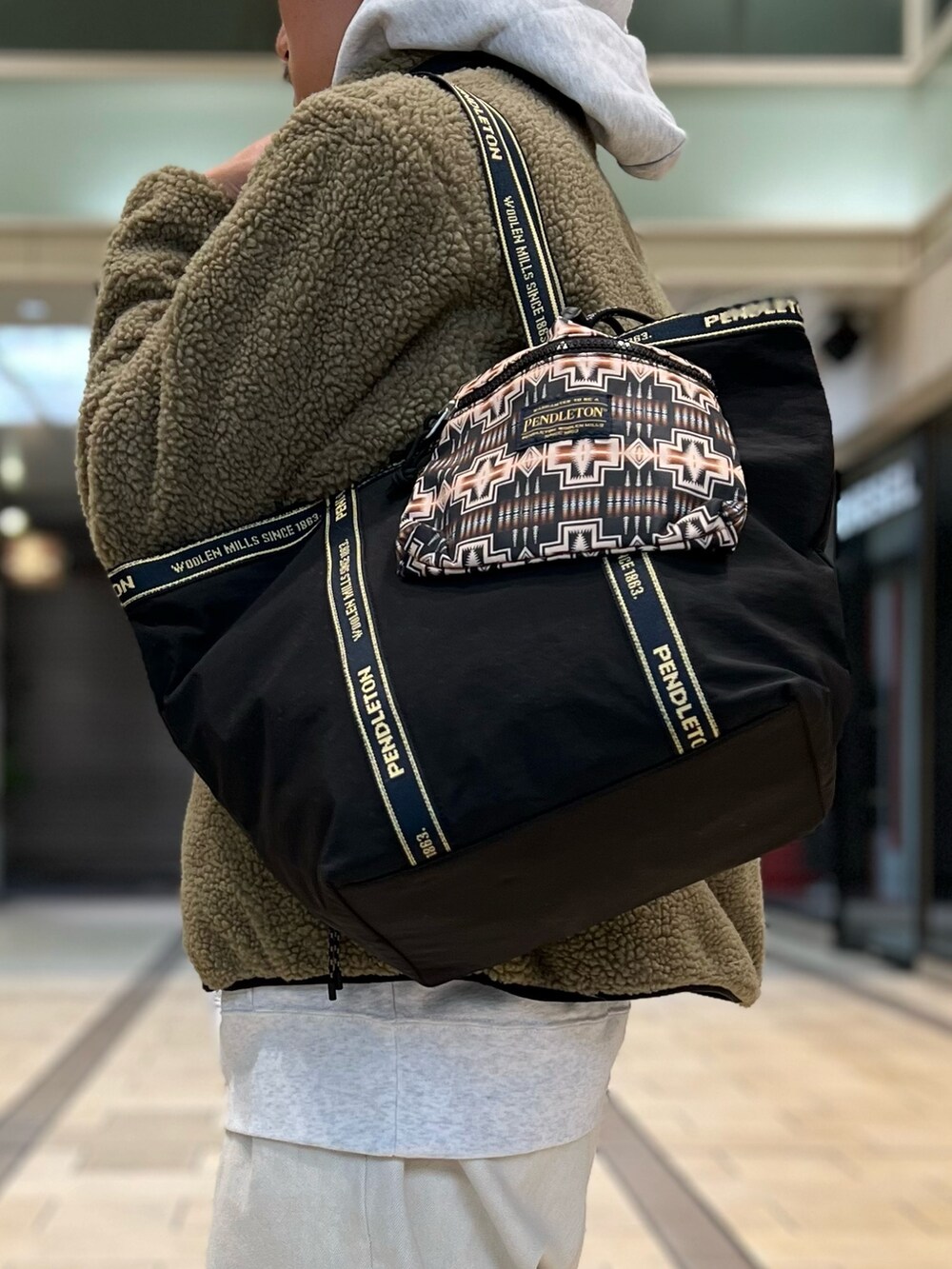 ベージュ系のダウンジャケット/コート、グレー系のパーカー、ブラック系のトートバッグを着用したメンズの秋コーディネートの7枚目の写真