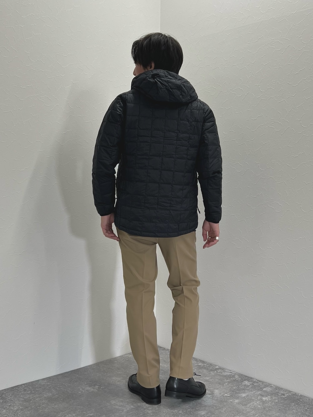 グレー系のニット/セーター、ブラック系のダウンジャケット/コート、ベージュ系のチノパンツを着用したメンズの秋コーディネートの5枚目の写真