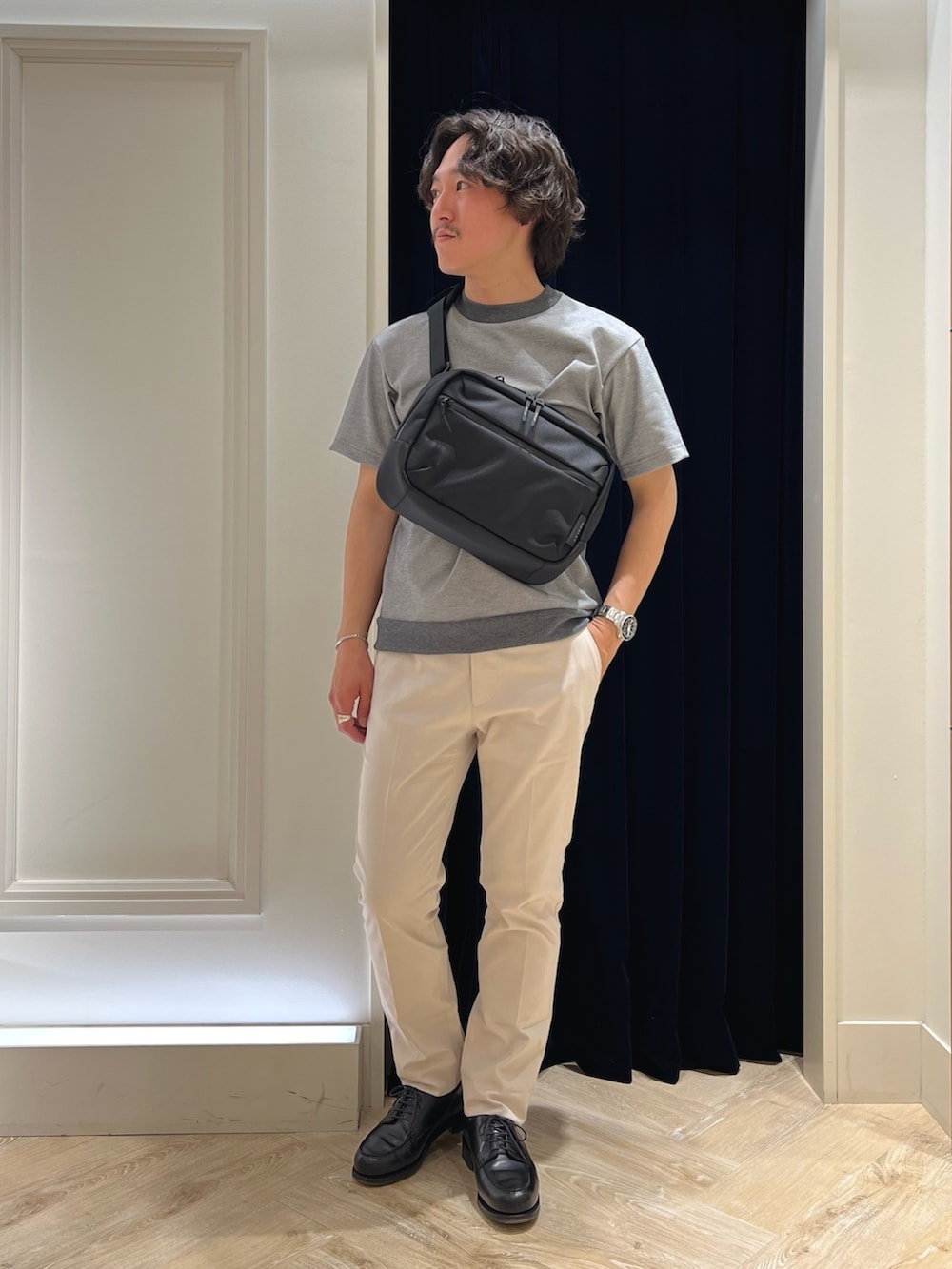 グレー系のTシャツ/カットソー、ブラック系のショルダーバッグ、ホワイト系のチノパンツを着用したメンズの春コーディネートの2枚目の写真