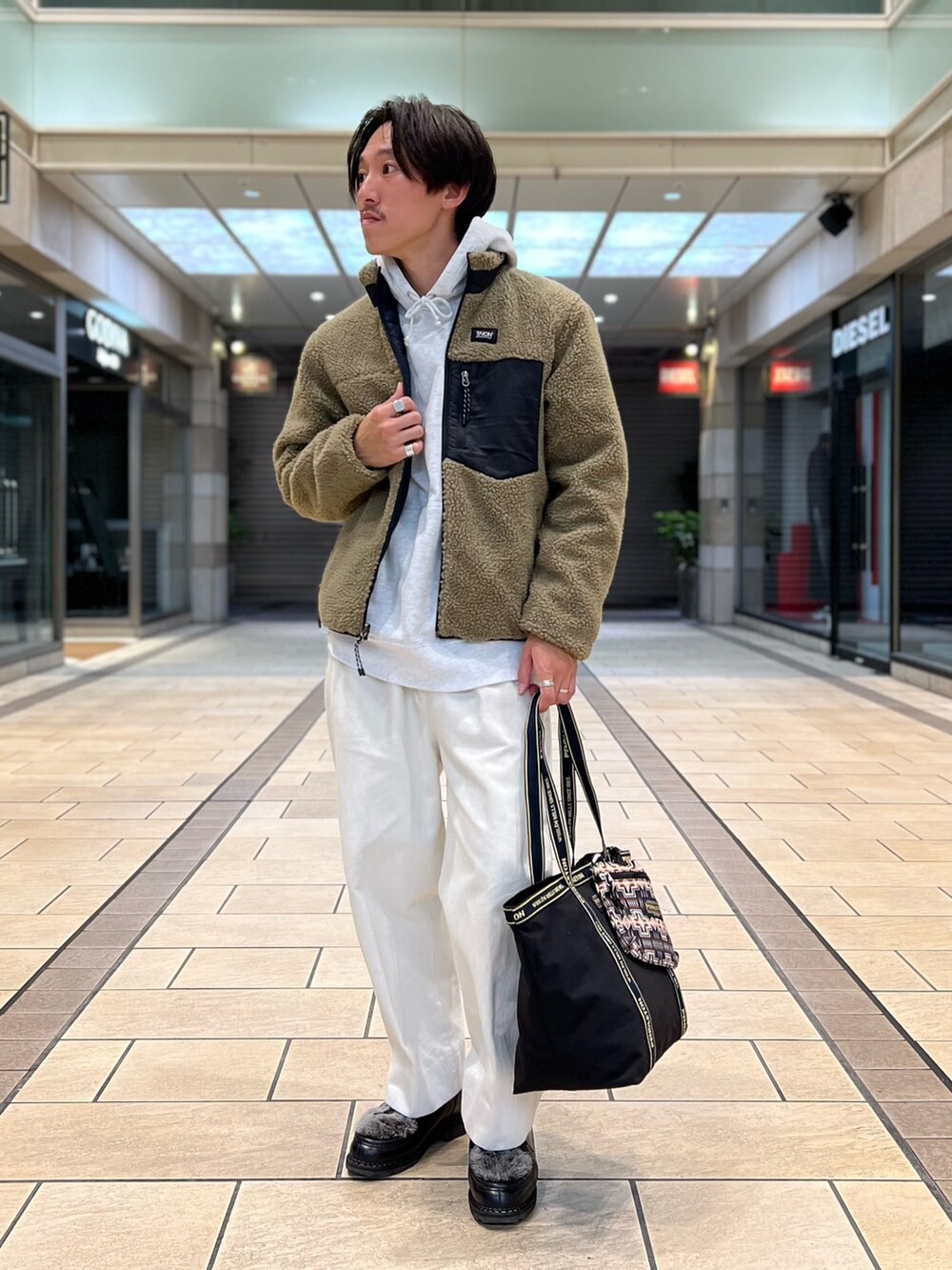 ベージュ系のダウンジャケット/コート、グレー系のパーカー、ブラック系のトートバッグを着用したメンズの秋コーディネートの2枚目の写真