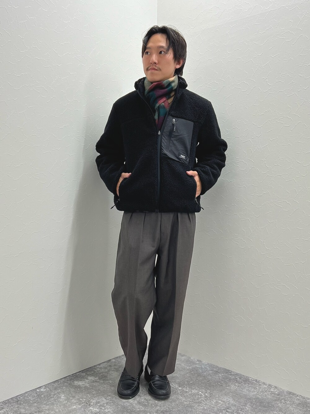 ブラック系のブルゾン、ベージュ系のニット/セーター、グレー系のマフラーを着用したメンズの秋コーディネートの2枚目の写真