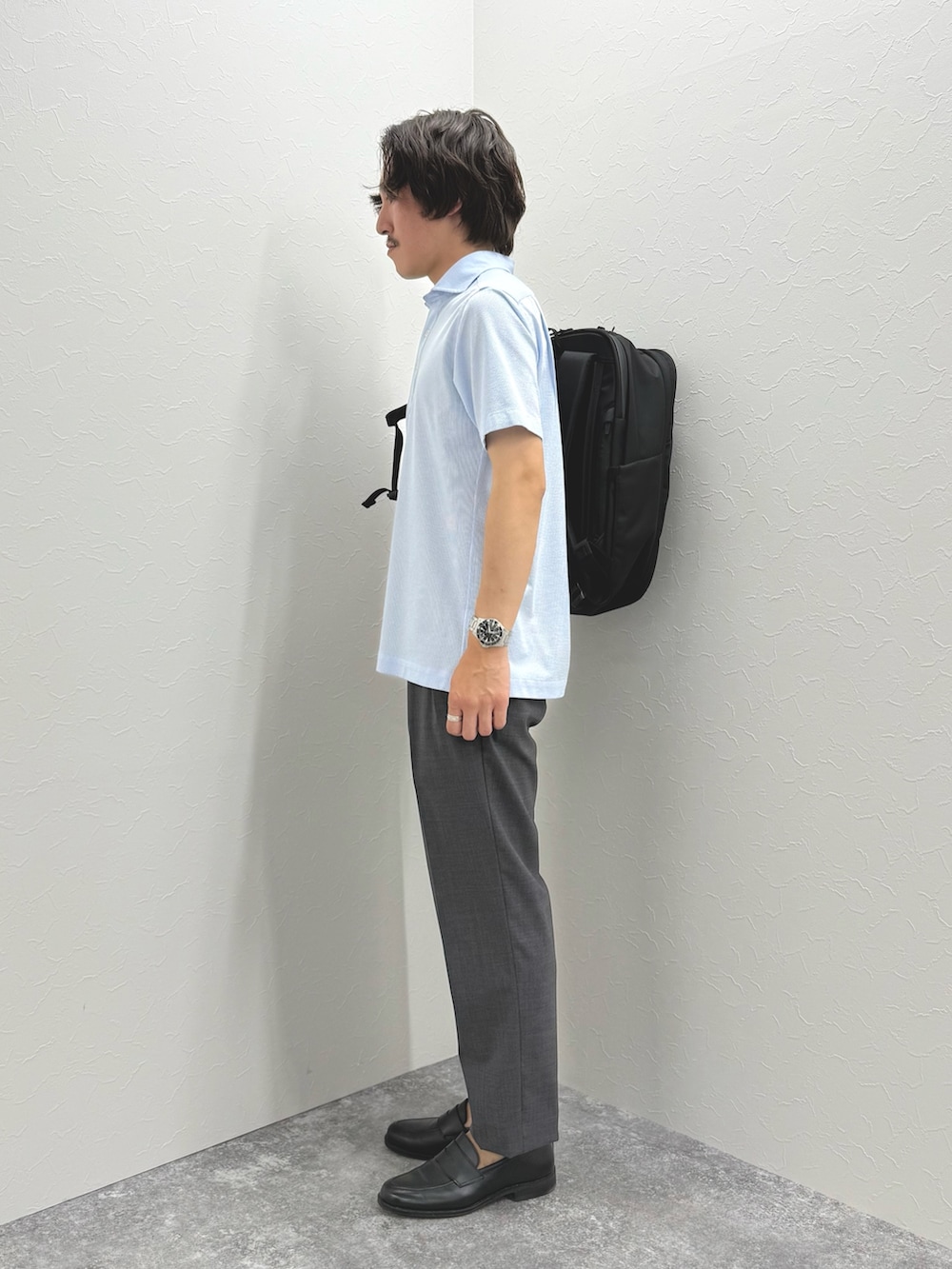 ブルー系のポロシャツ、グレー系のスラックス、ブラック系のバックパック/リュックを着用したメンズの春コーディネートの6枚目の写真