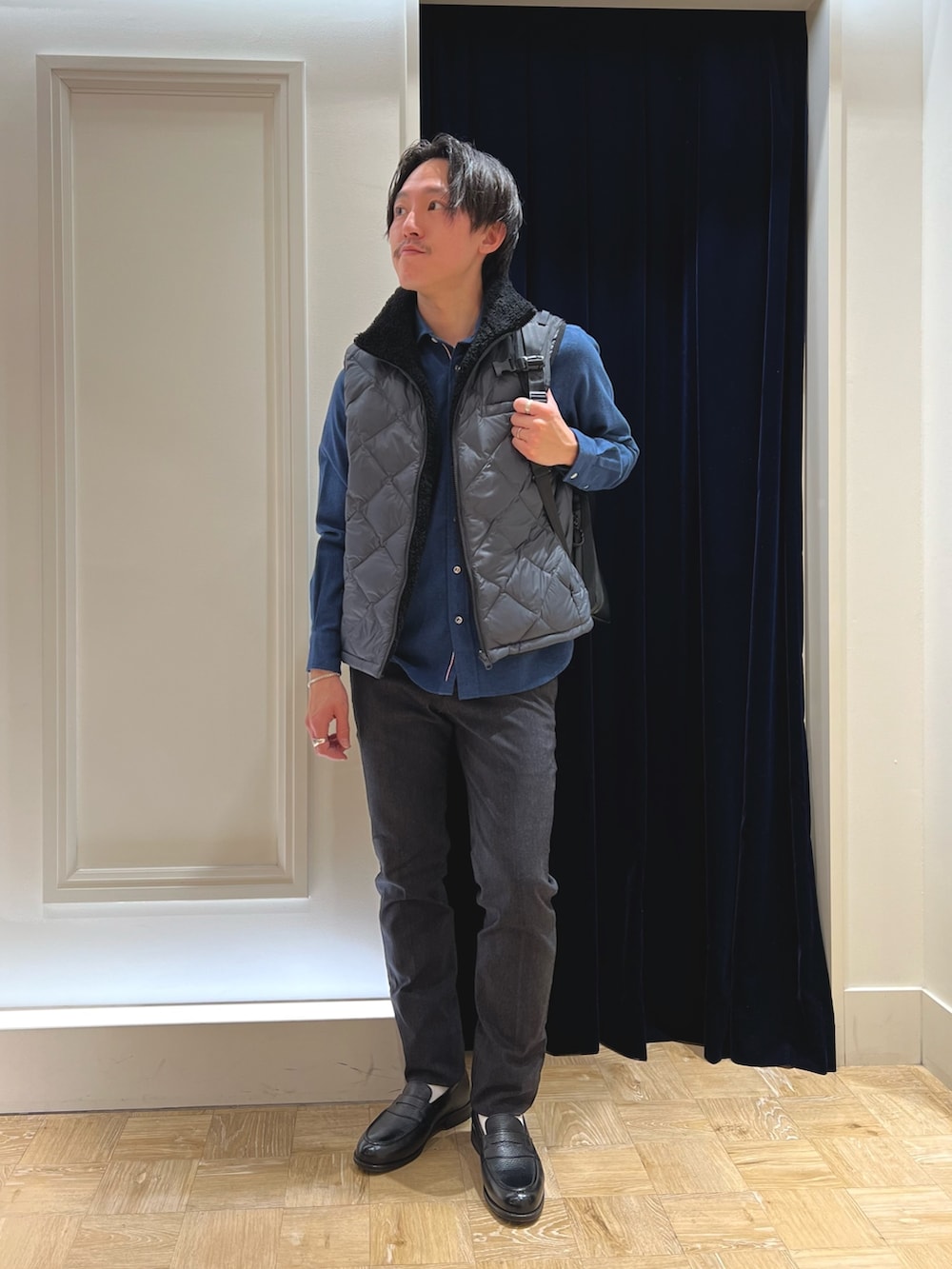 グレー系のダウンベスト、ブルー系のシャツ/ブラウス、ブラック系のバックパック/リュックを着用したメンズの冬コーディネートの3枚目の写真