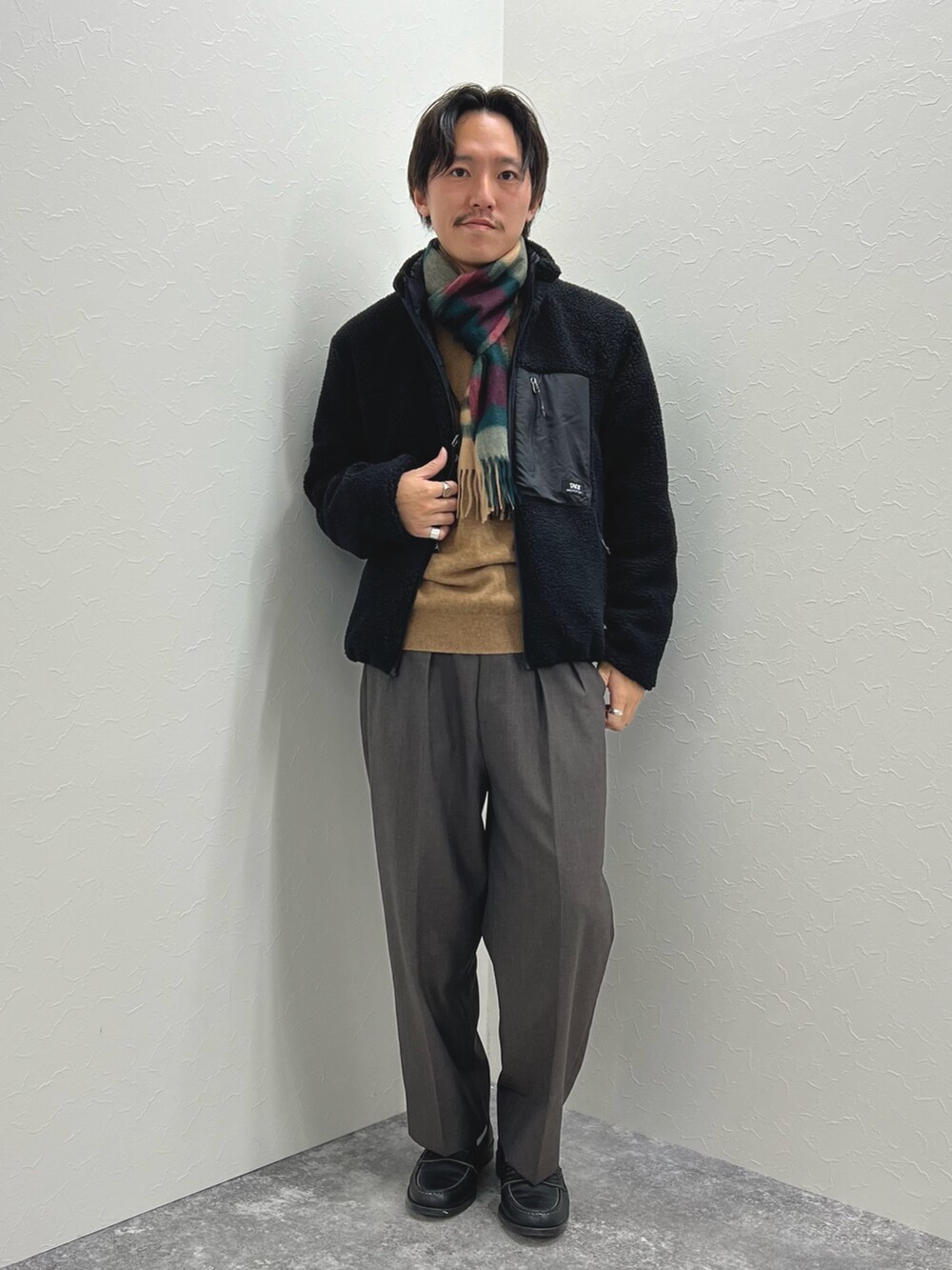 ブラック系のブルゾン、ベージュ系のニット/セーター、グレー系のマフラーを着用したメンズの秋コーディネートの4枚目の写真