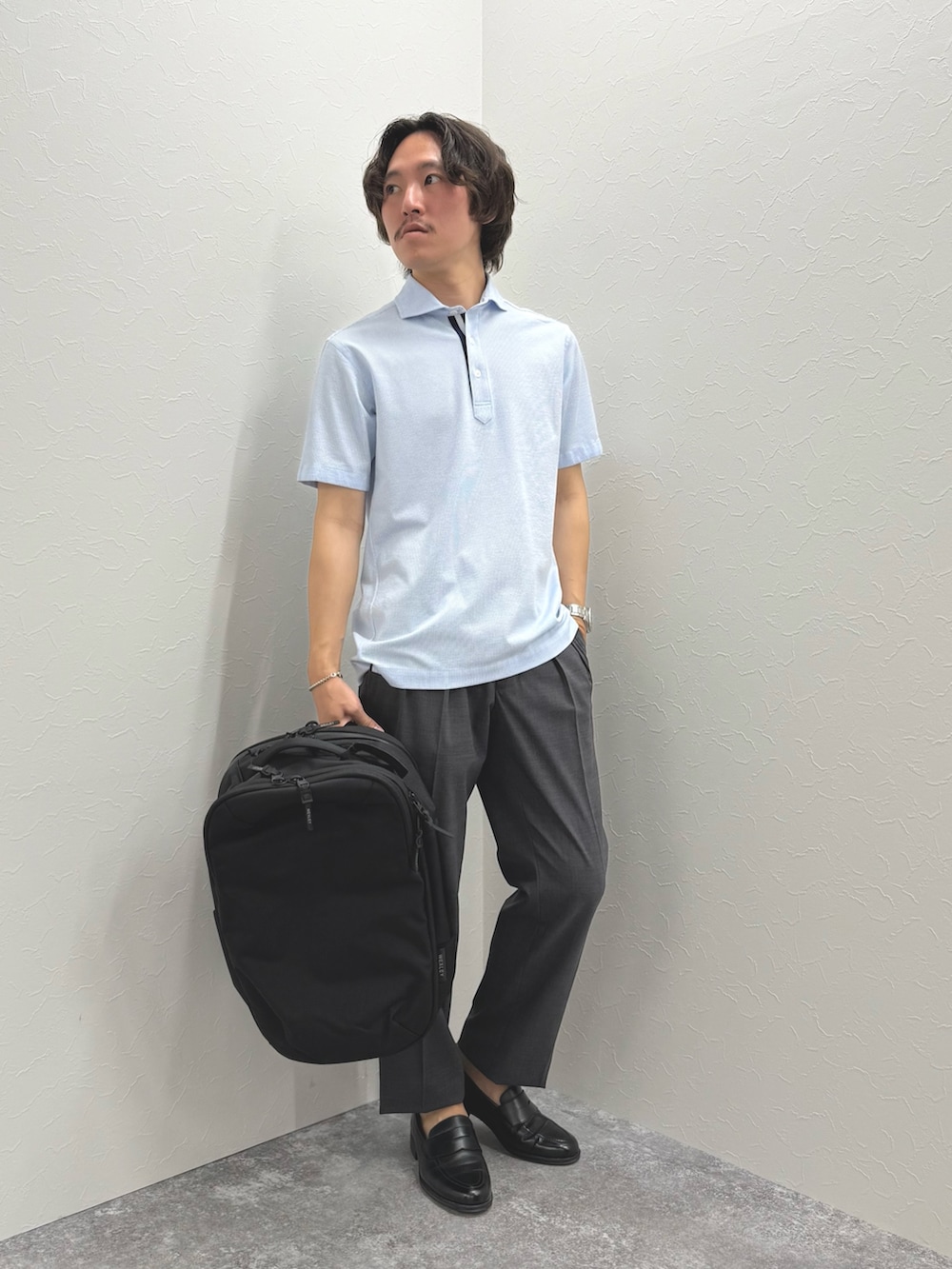 ブルー系のポロシャツ、グレー系のスラックス、ブラック系のバックパック/リュックを着用したメンズの春コーディネートの2枚目の写真